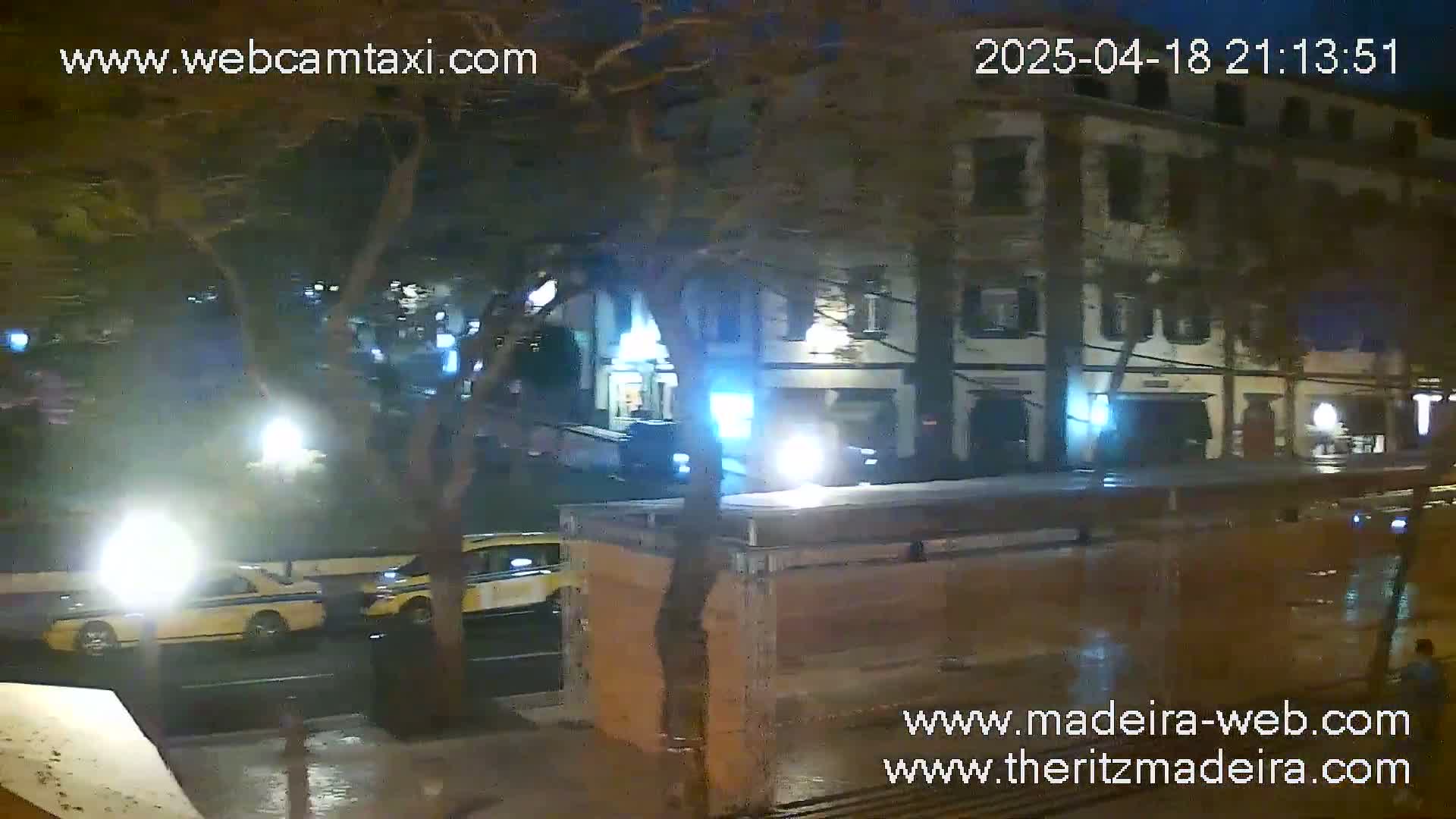 At night, under wet conditions, two yellow taxis are visible on a street in front of a multi-story building.