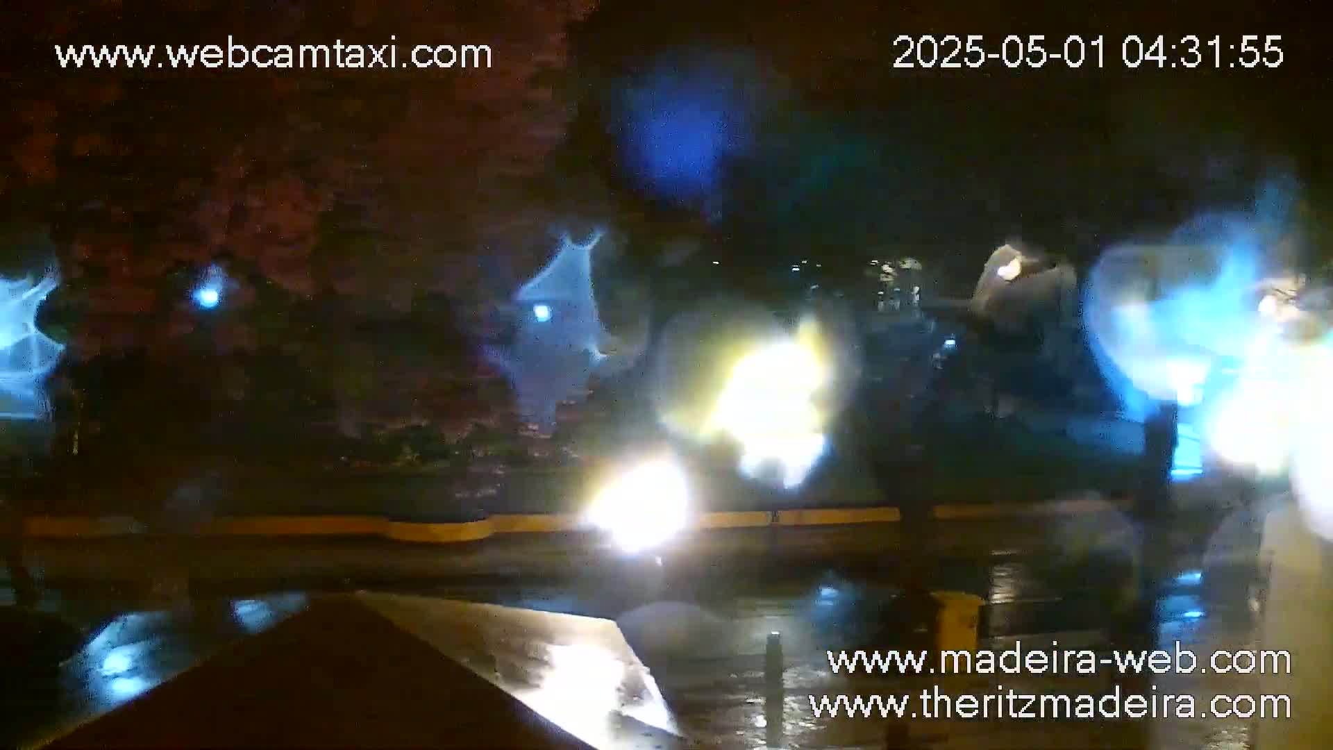 A nighttime, rainy scene shows blurry figures and bright lights reflecting on a wet surface.