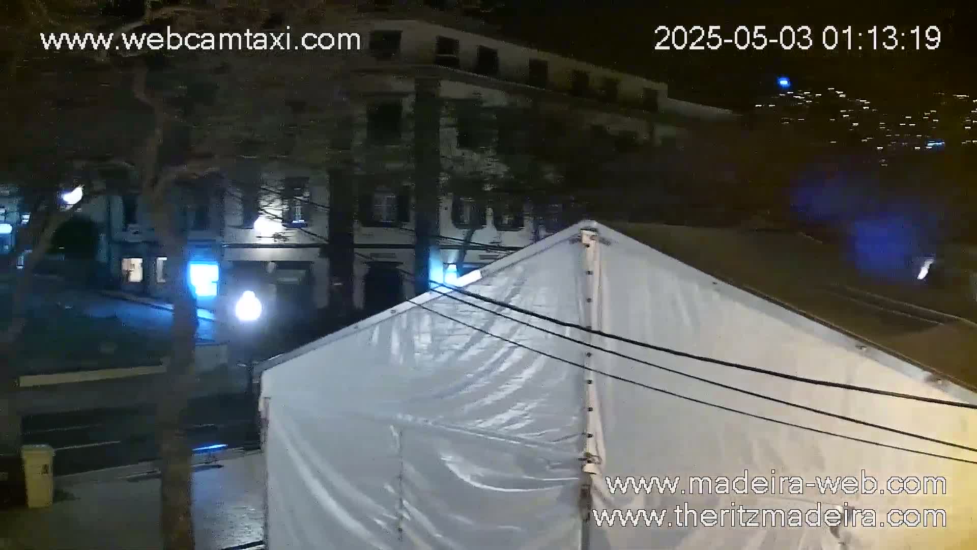 A large white tent sits in a city street at night, illuminated by streetlights and distant building lights.