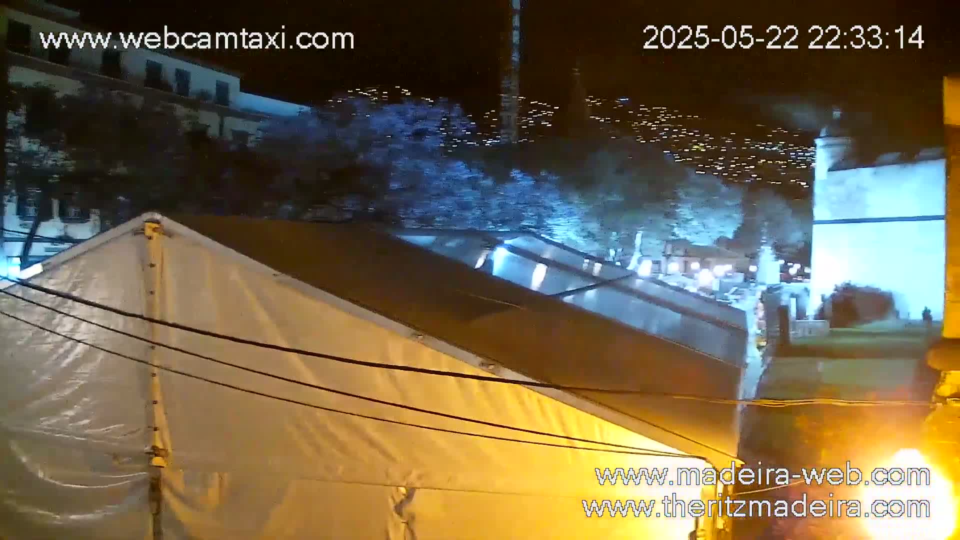 At night, a large white tent is partially visible under a dark sky illuminated by distant lights.