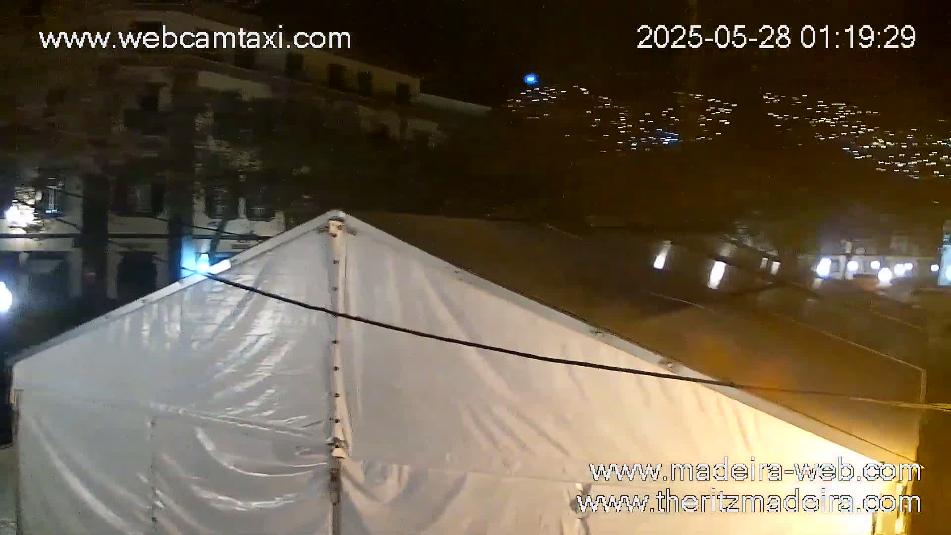 A large white tent is seen at night, in front of a building with lights illuminating the scene.