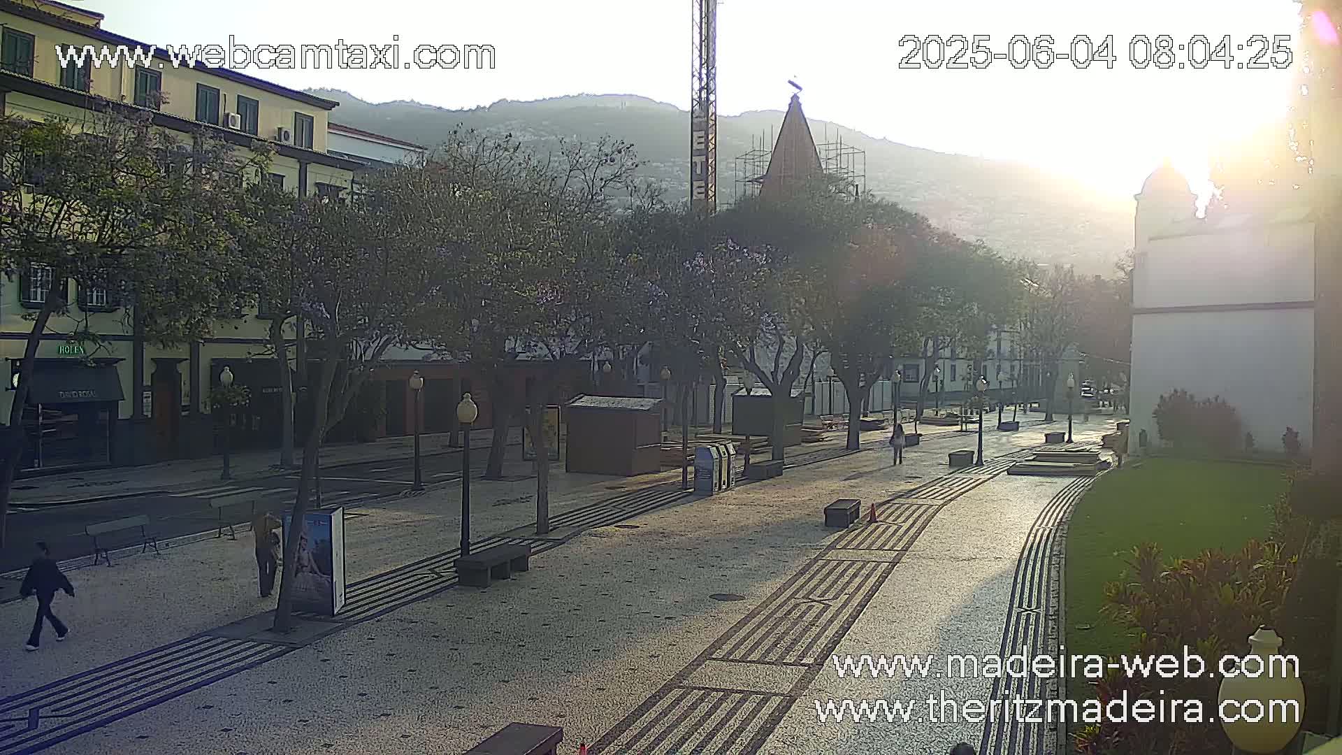 A sunlit plaza with tree-lined streets and buildings, under a hazy morning sky.