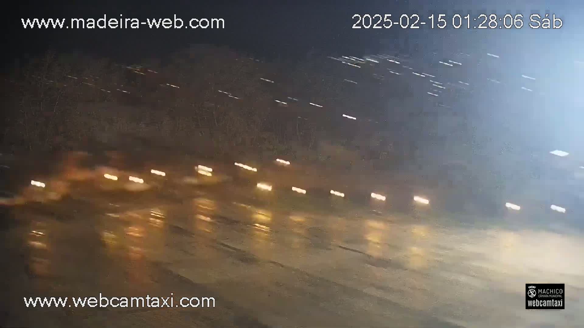 A wet road at night is shown with blurred headlights of several vehicles driving in the distance under a light rain.
