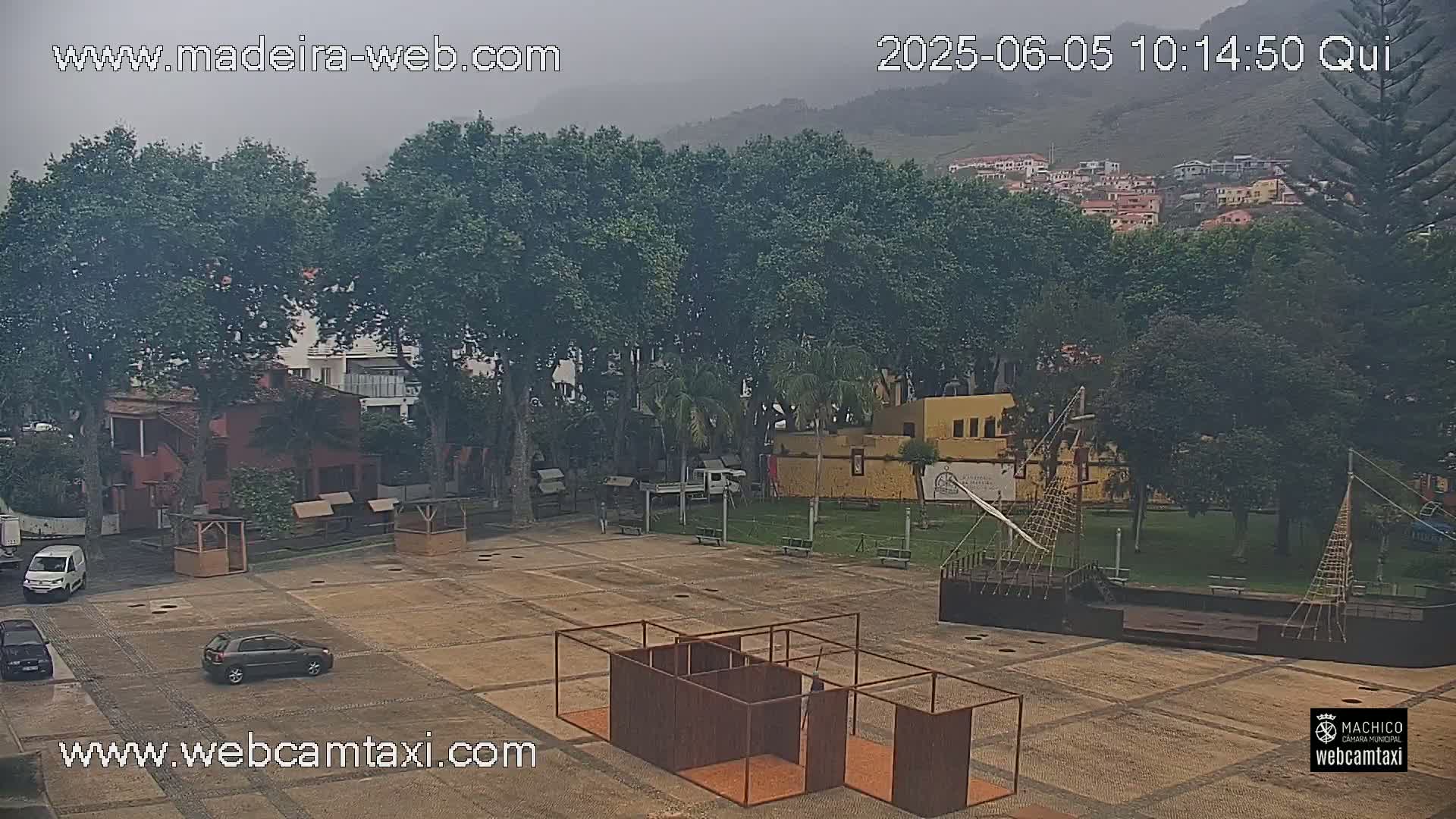 A hazy, overcast day reveals a plaza with a few cars, several trees, some small buildings, and a model ship in the foreground.
