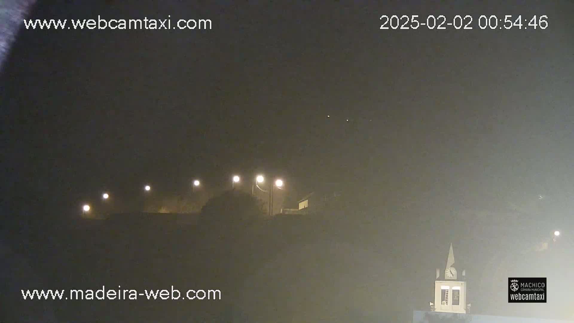 A nighttime view of a hazy, dimly lit landscape with several streetlights and a building with a steeple in the distance.