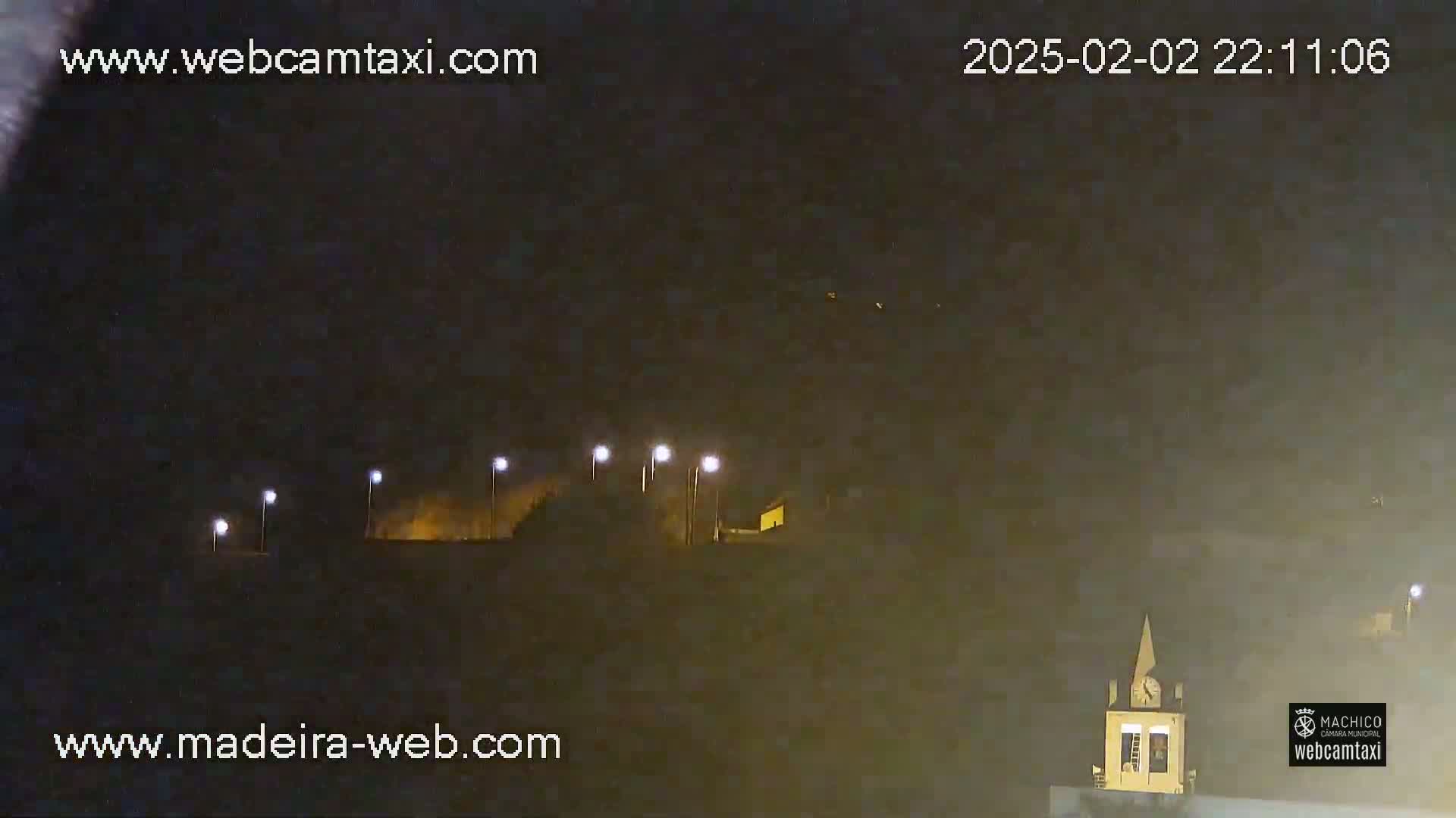 At night, under a dark sky, several lights illuminate a hilltop with a building and a steeple.
