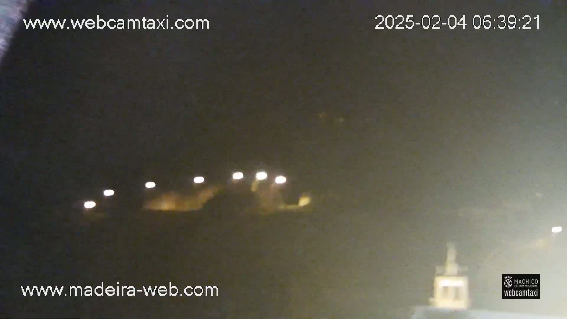 A nighttime, blurry view of a dark landscape with several small lights visible in the distance.