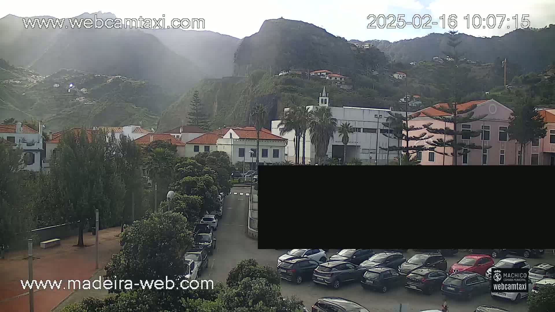 A hazy view of a town nestled in a mountainous region, with several cars parked along a street and buildings visible.