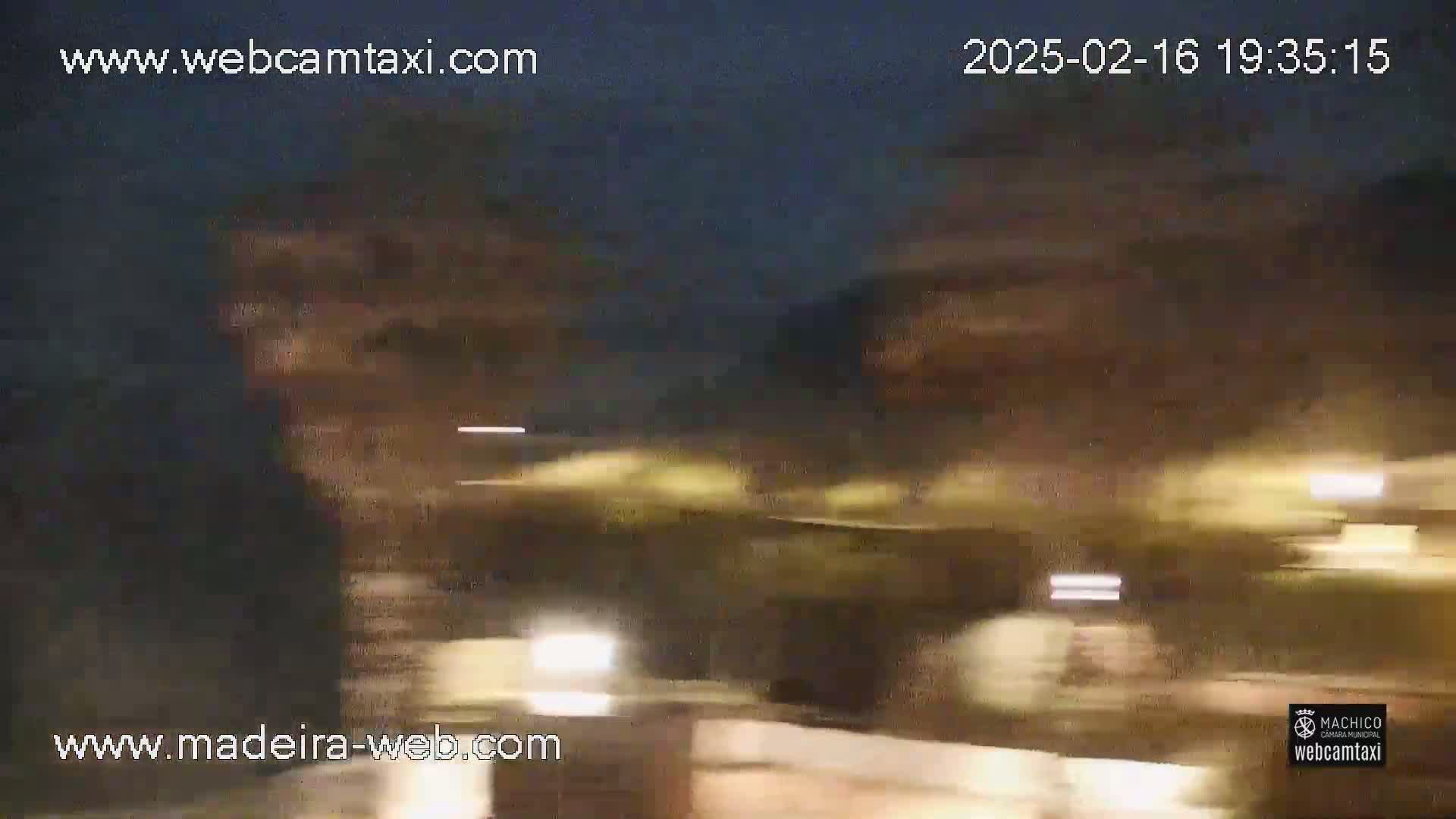 A nighttime, blurry view of traffic lights and vehicles moving along a road under a dark sky.
