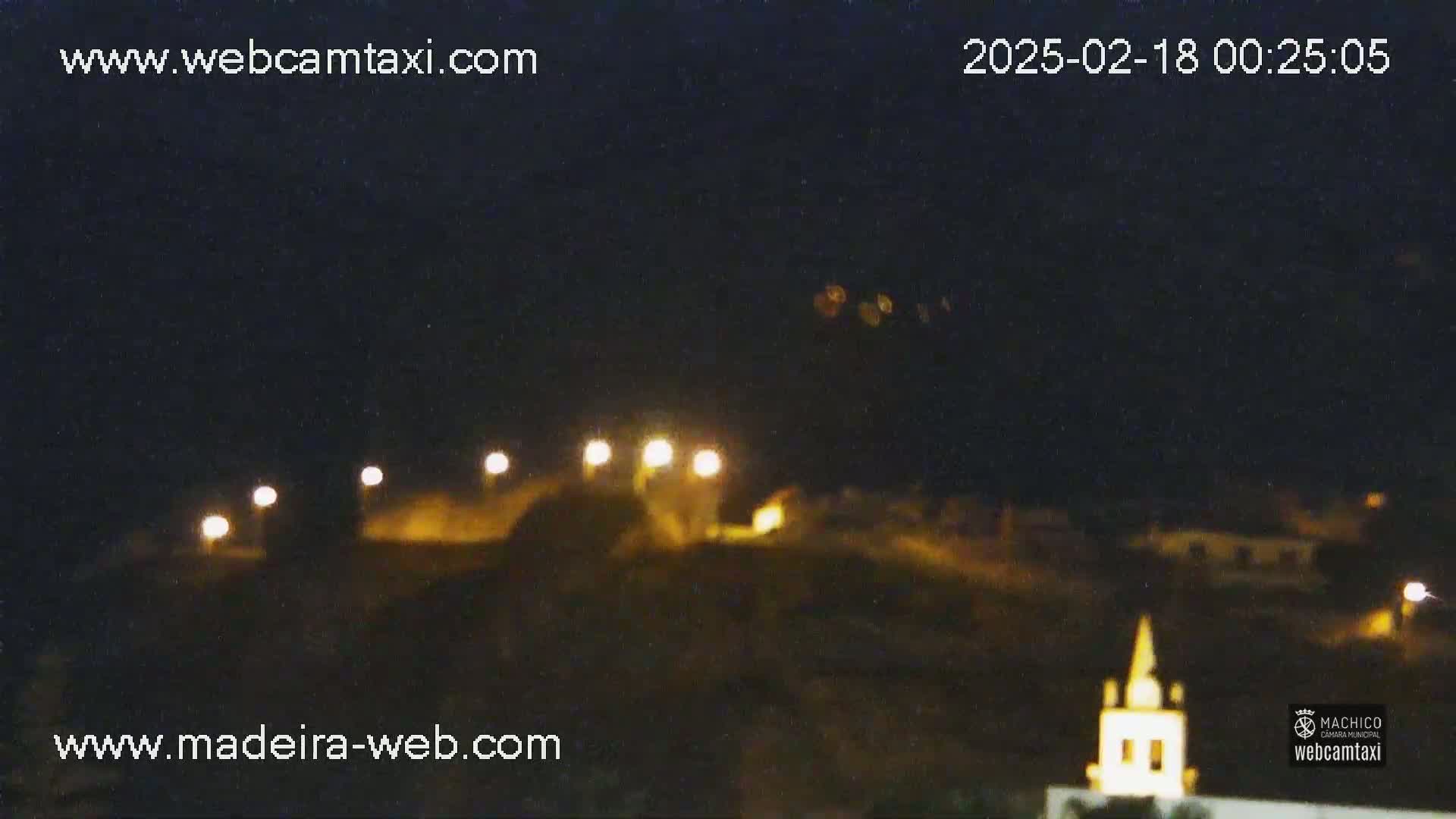 A nighttime view of a hilltop with illuminated buildings and a small church, under a clear, dark sky.