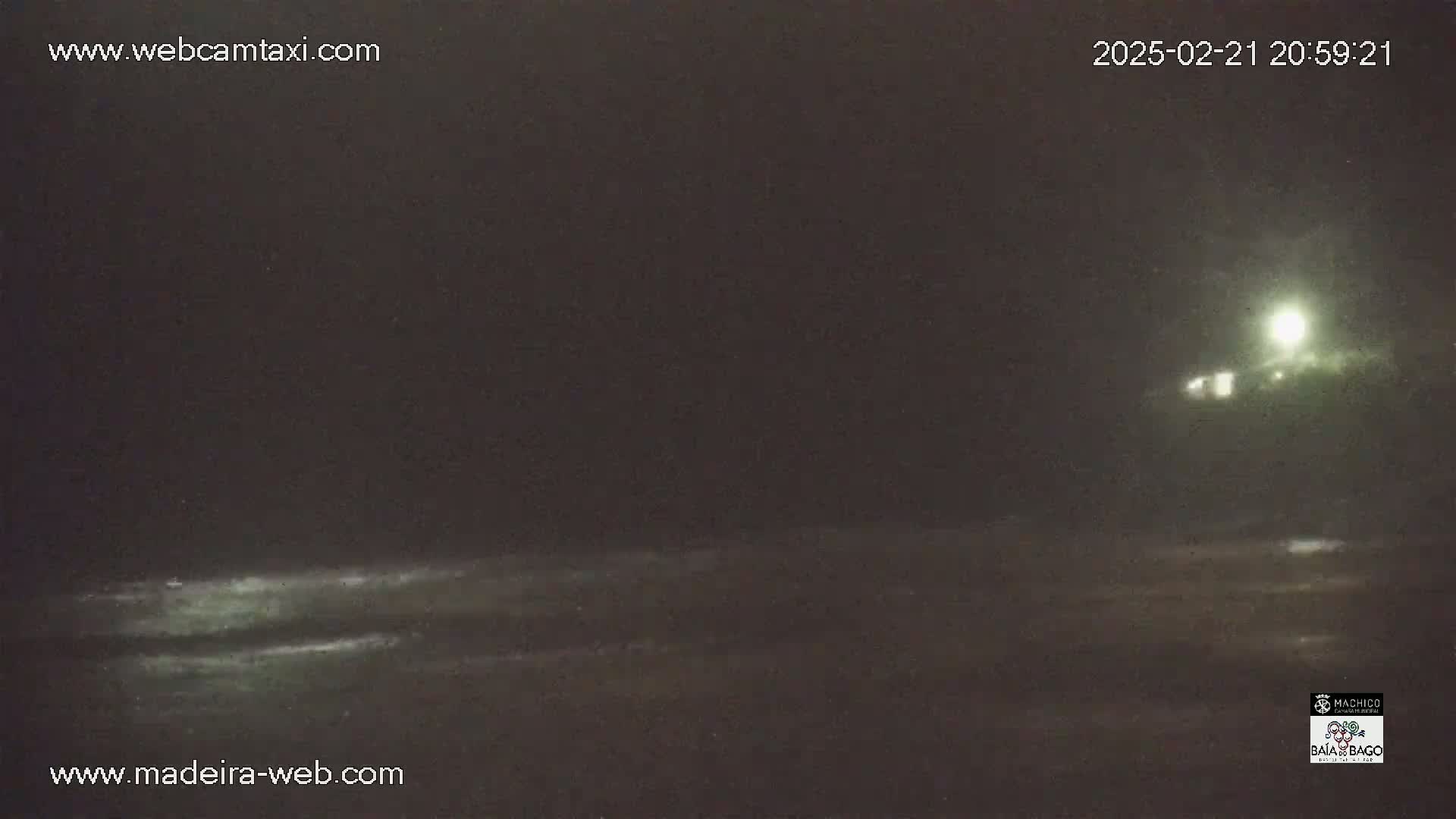 A nighttime, low-light view of a dark ocean with a faintly lit shoreline in the distance.