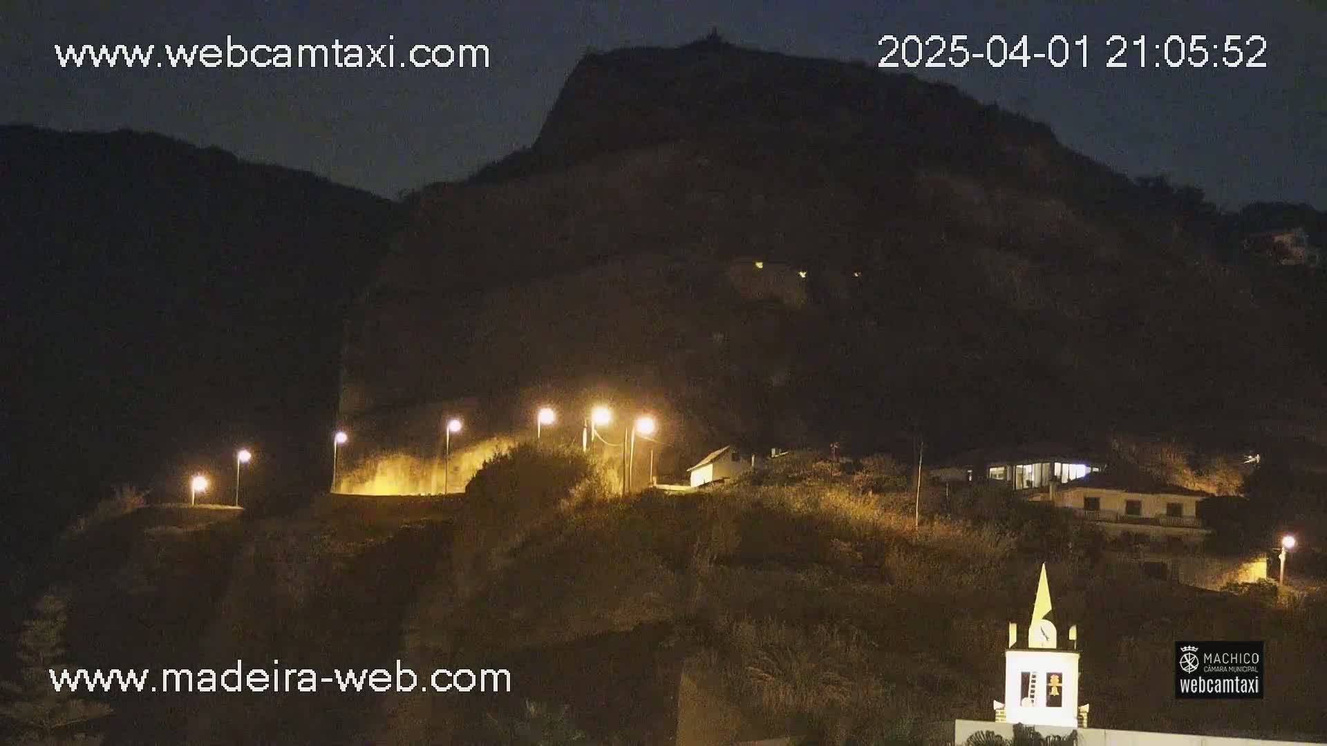A nighttime view of a hill illuminated by streetlights, featuring buildings and a steeple, under a clear, dark sky.