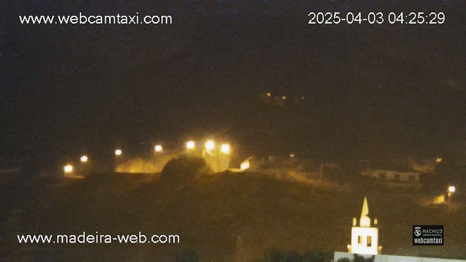 A nighttime long shot shows a dimly lit hillside with a few buildings and lights, under a dark, clear sky.