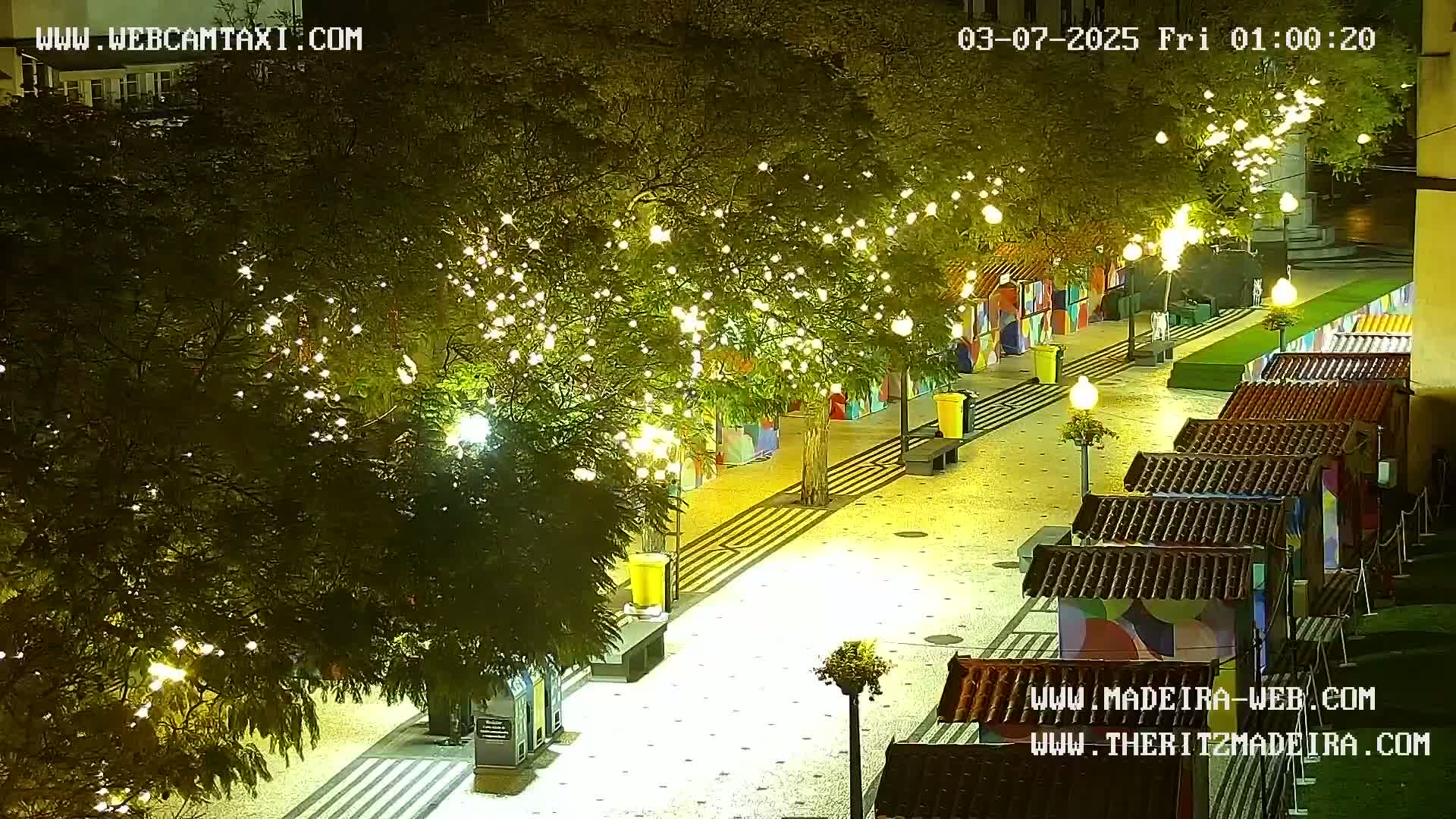 A nighttime view of a paved walkway lined with small, colorful shops and trees decorated with string lights.