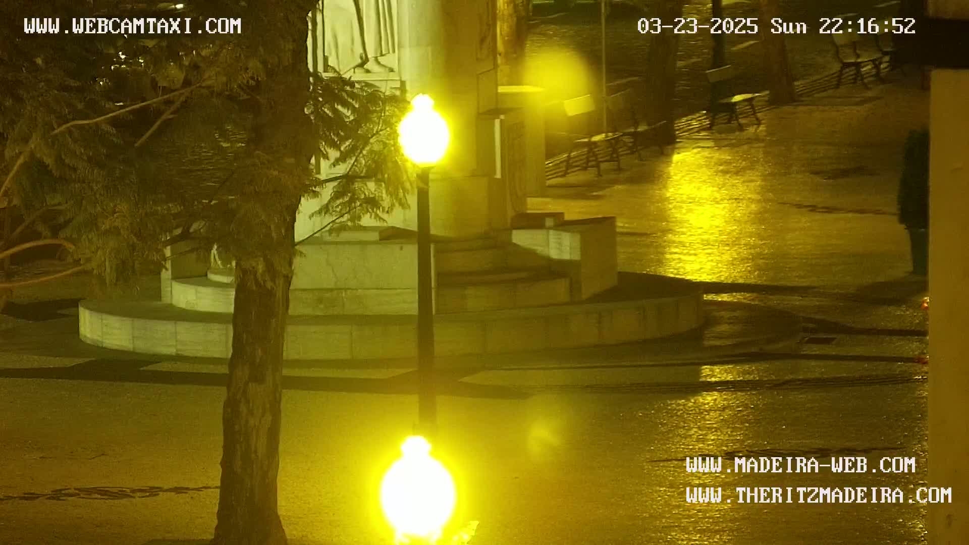 A wet, nighttime scene shows a stone structure illuminated by bright yellow streetlights.