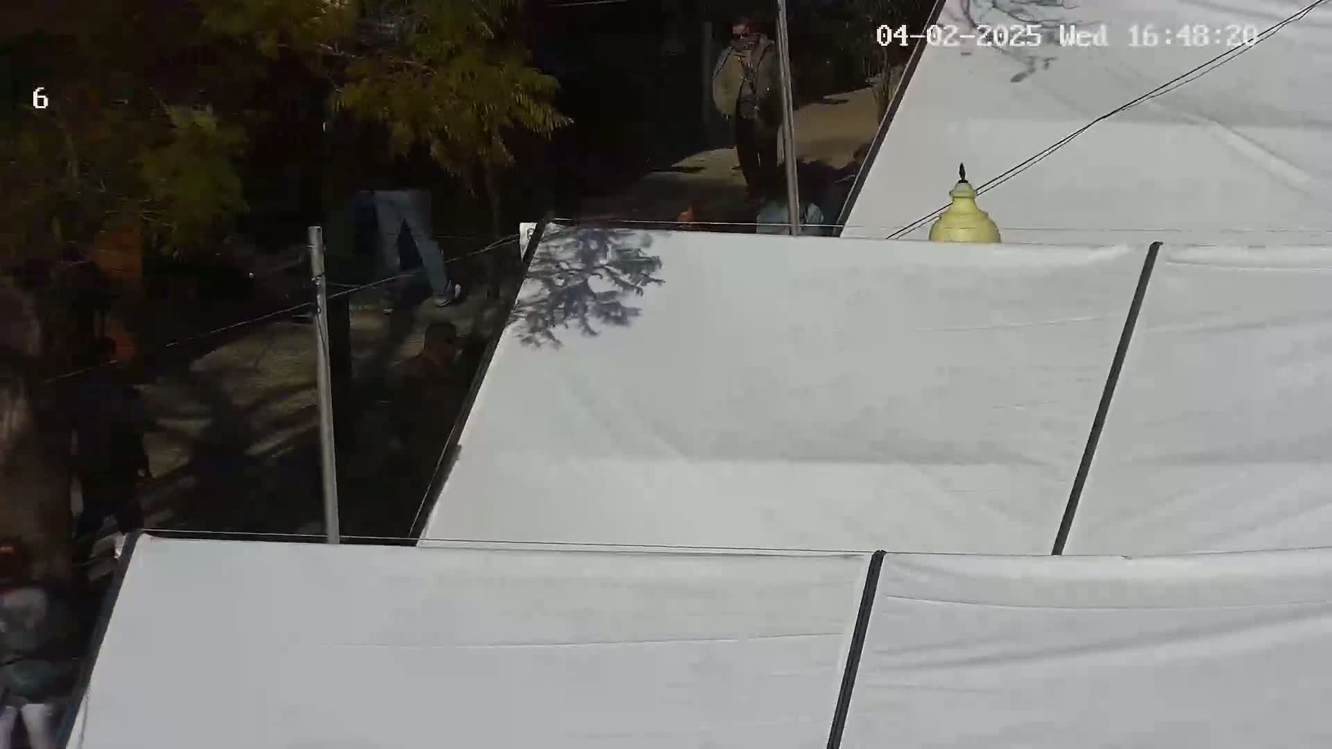 A high-angle view shows several people near a large white fabric structure on a sunny day.