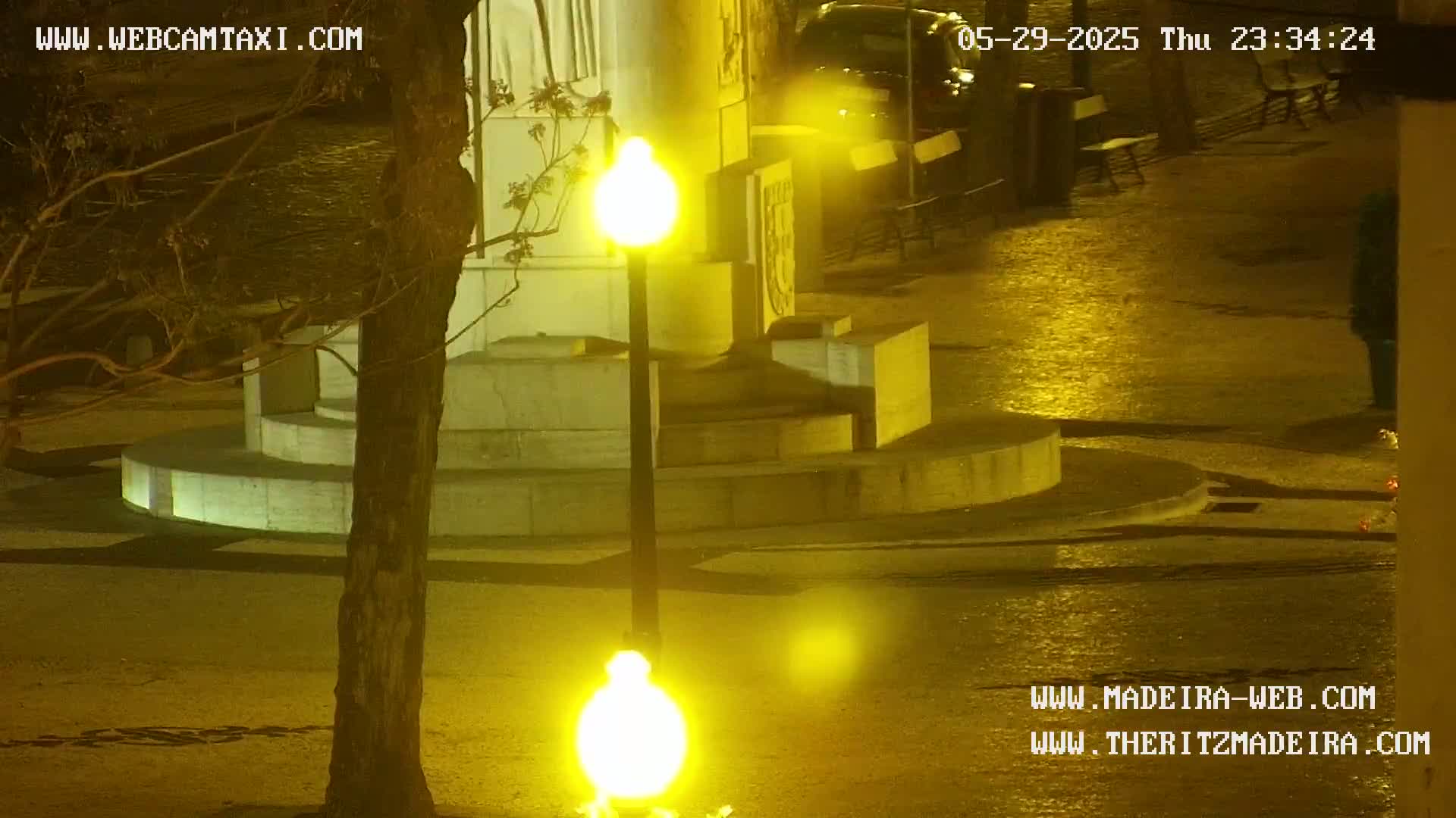 A nighttime, wet, outdoor scene shows a stone monument illuminated by bright streetlights.