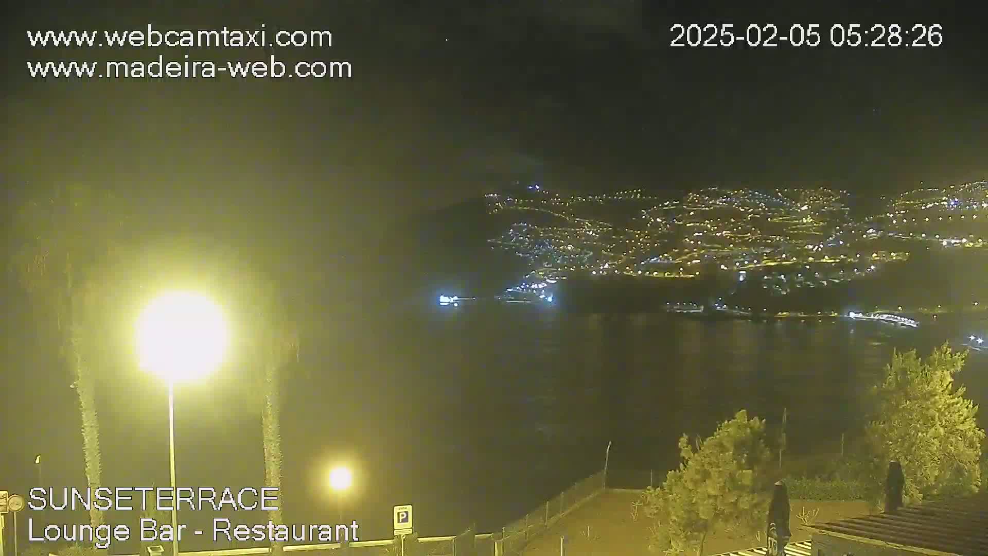 A nighttime view overlooking a city illuminated by lights along a dark body of water, under a clear sky.
