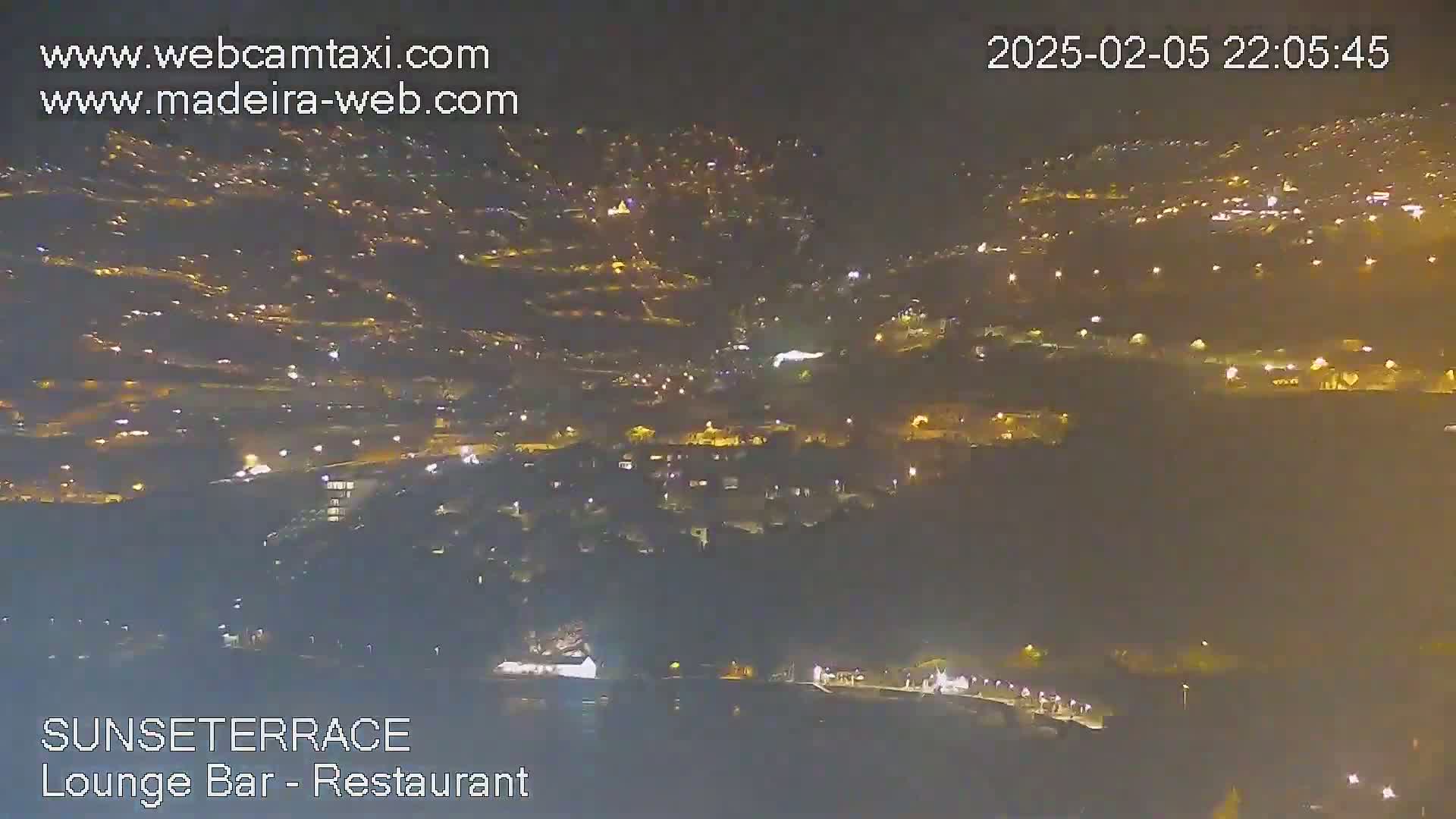 A nighttime, high-angle view shows a hillside town illuminated by numerous lights.