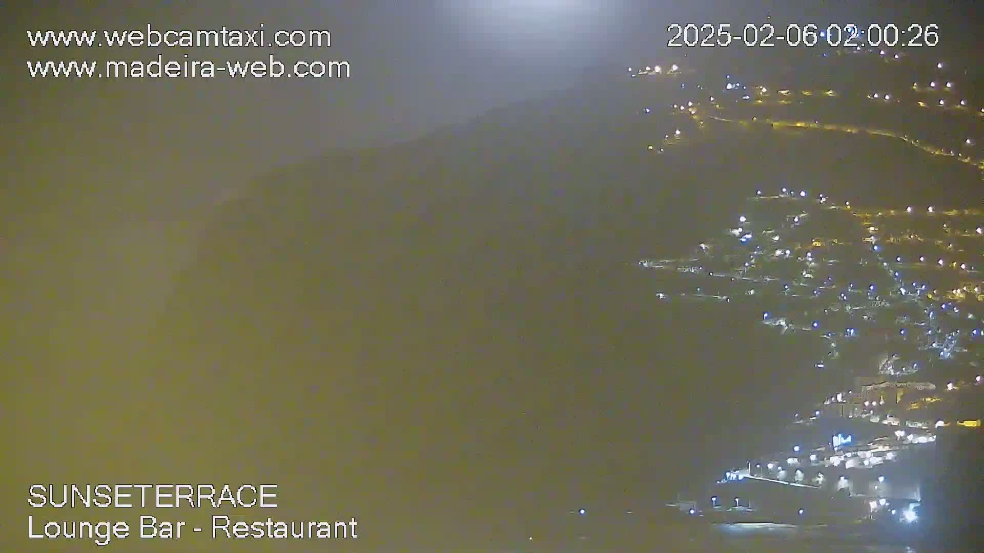 A hazy night scene shows a hillside town illuminated by many lights.