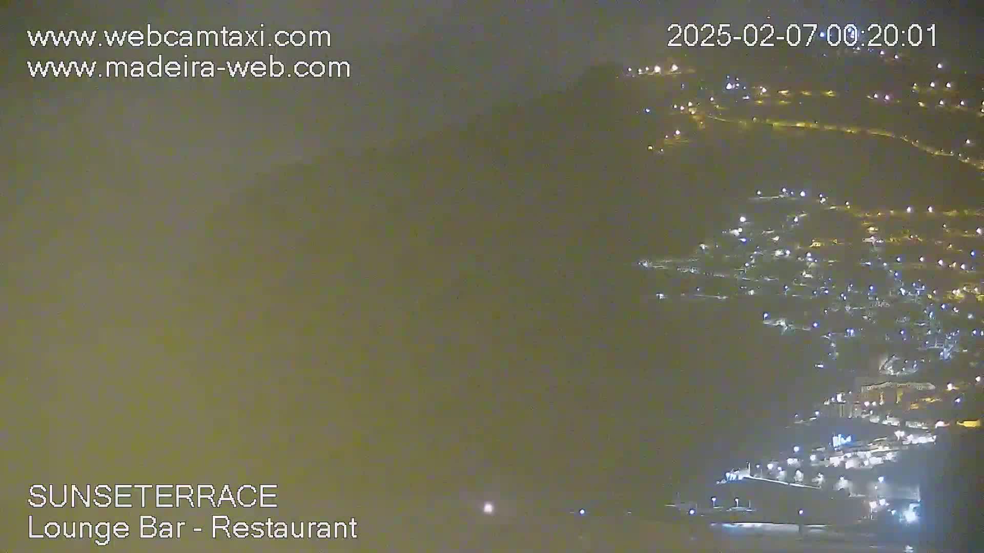 A night-time, hazy view of a hillside town illuminated by many lights.