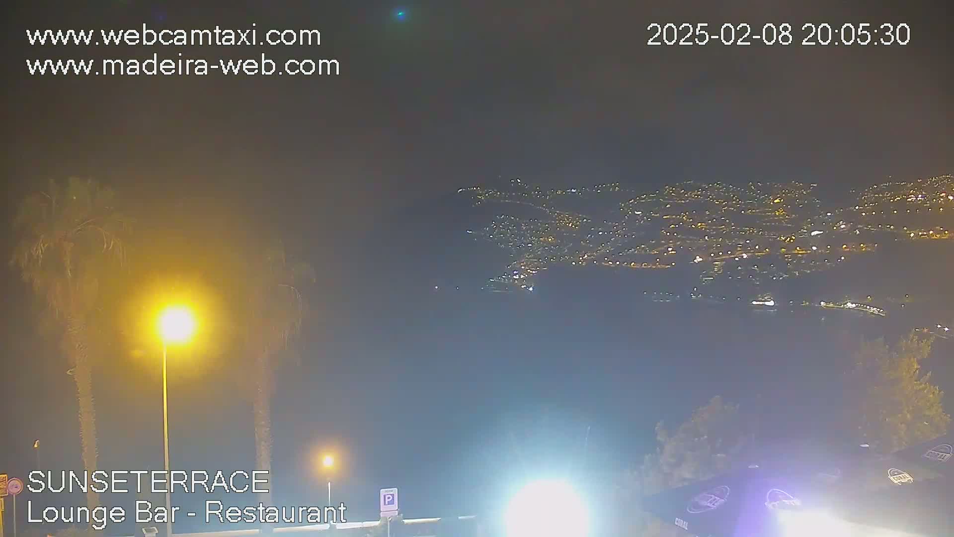 A nighttime, hazy view of a city illuminated by numerous lights stretches across a distant hillside, partially obscured by atmospheric conditions.