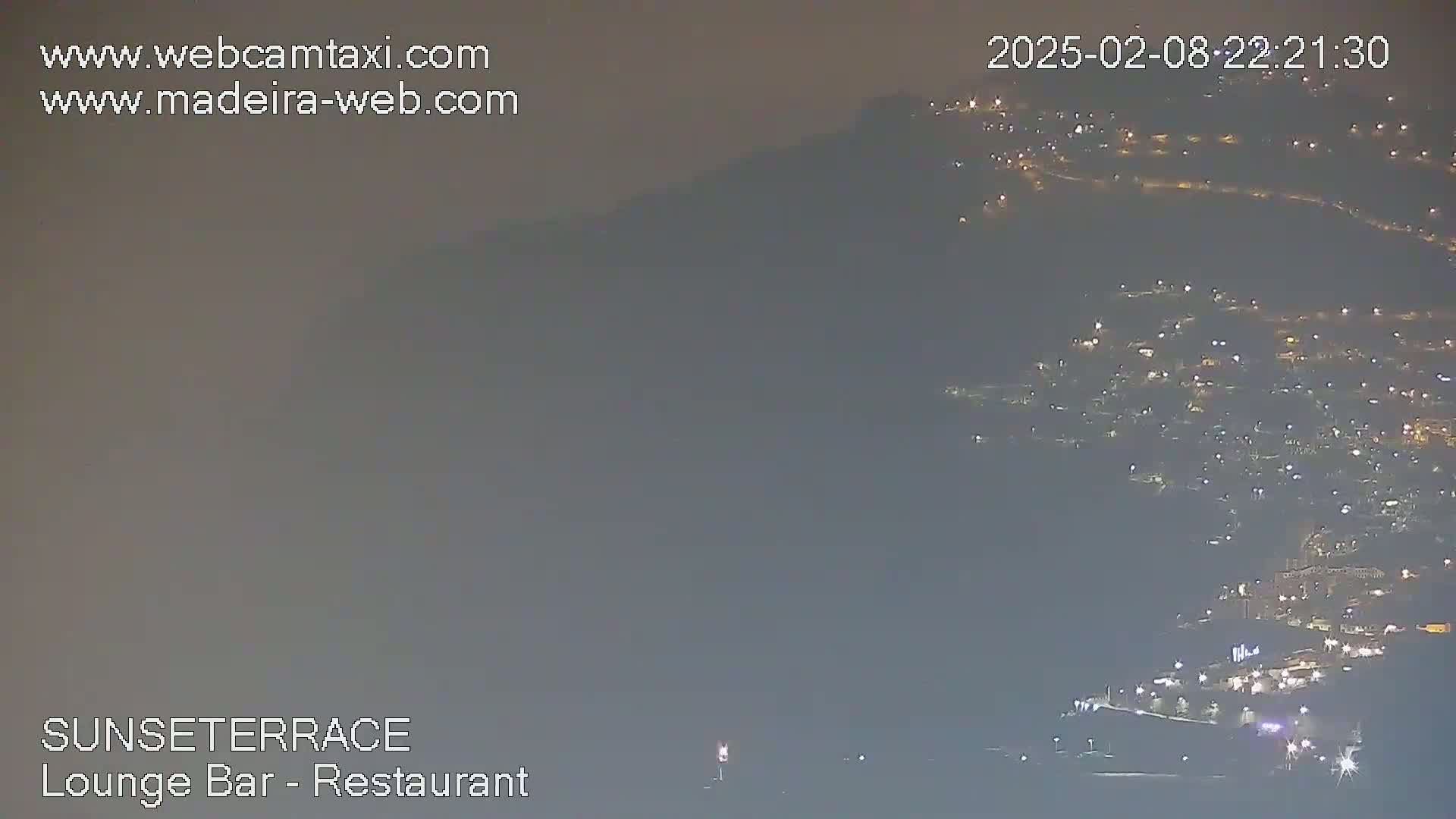 A hazy night scene shows a hillside town illuminated by many lights.