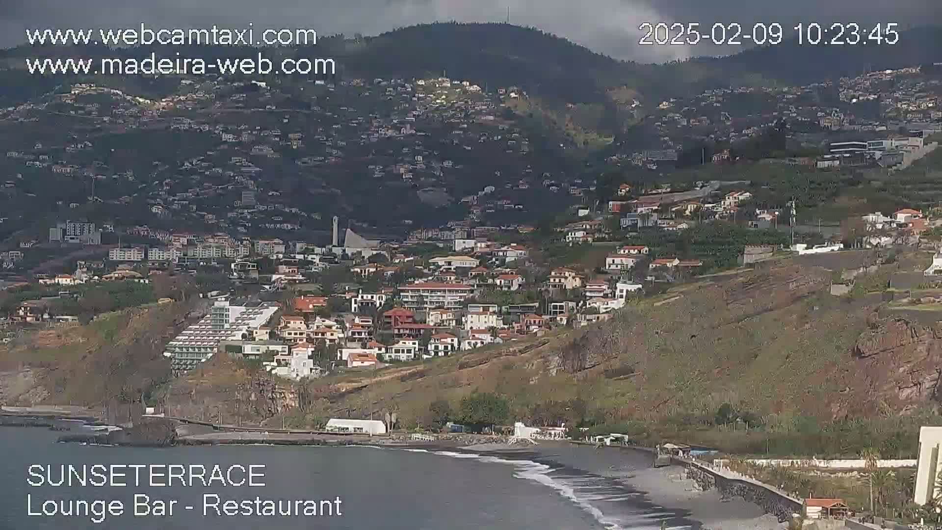 A coastal town built on a hillside overlooking a dark-sand beach on an overcast day.