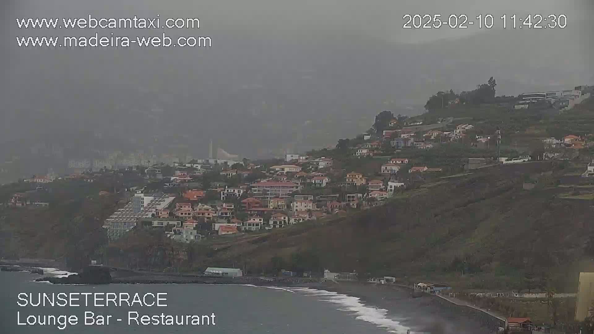 A hazy coastal town overlooks a dark, wavy ocean under overcast skies.