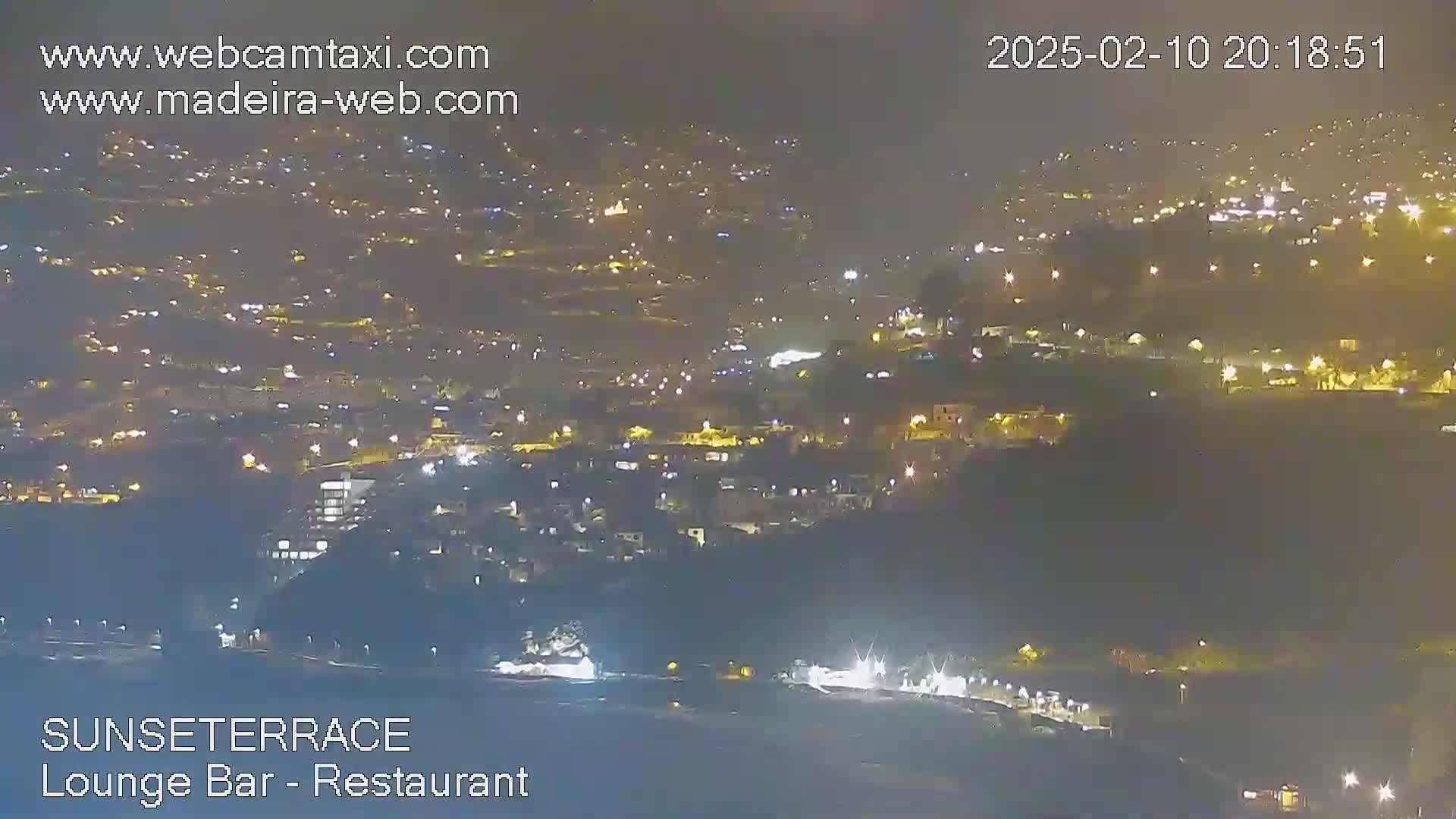 A nighttime, hazy view of a city sprawling across a hillside, illuminated by numerous lights.