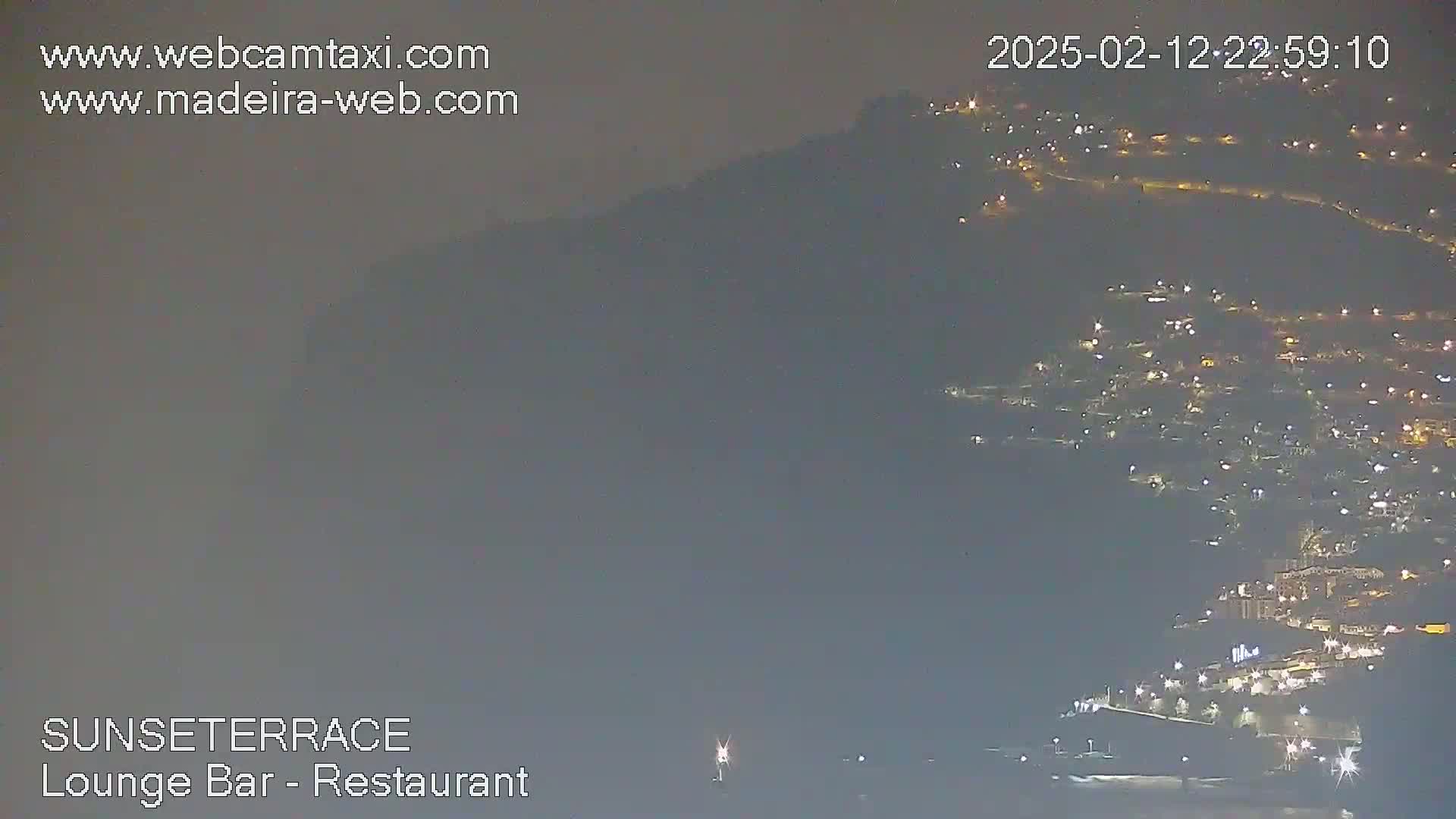 A hazy night view shows a hillside town with numerous lights, partially obscured by fog or mist.
