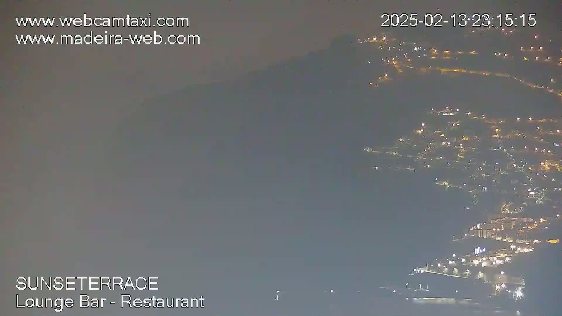 A nighttime, hazy view shows a hillside town with many lights illuminated against a dark sky.