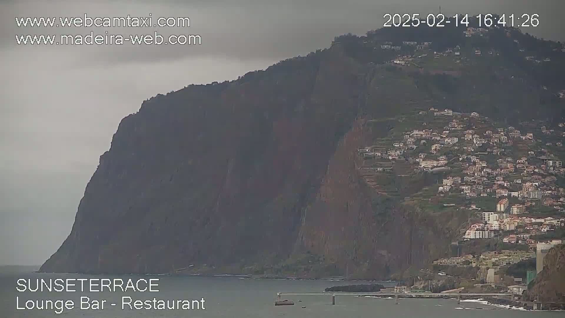A large, dark cliff overlooks a coastal town under an overcast sky.