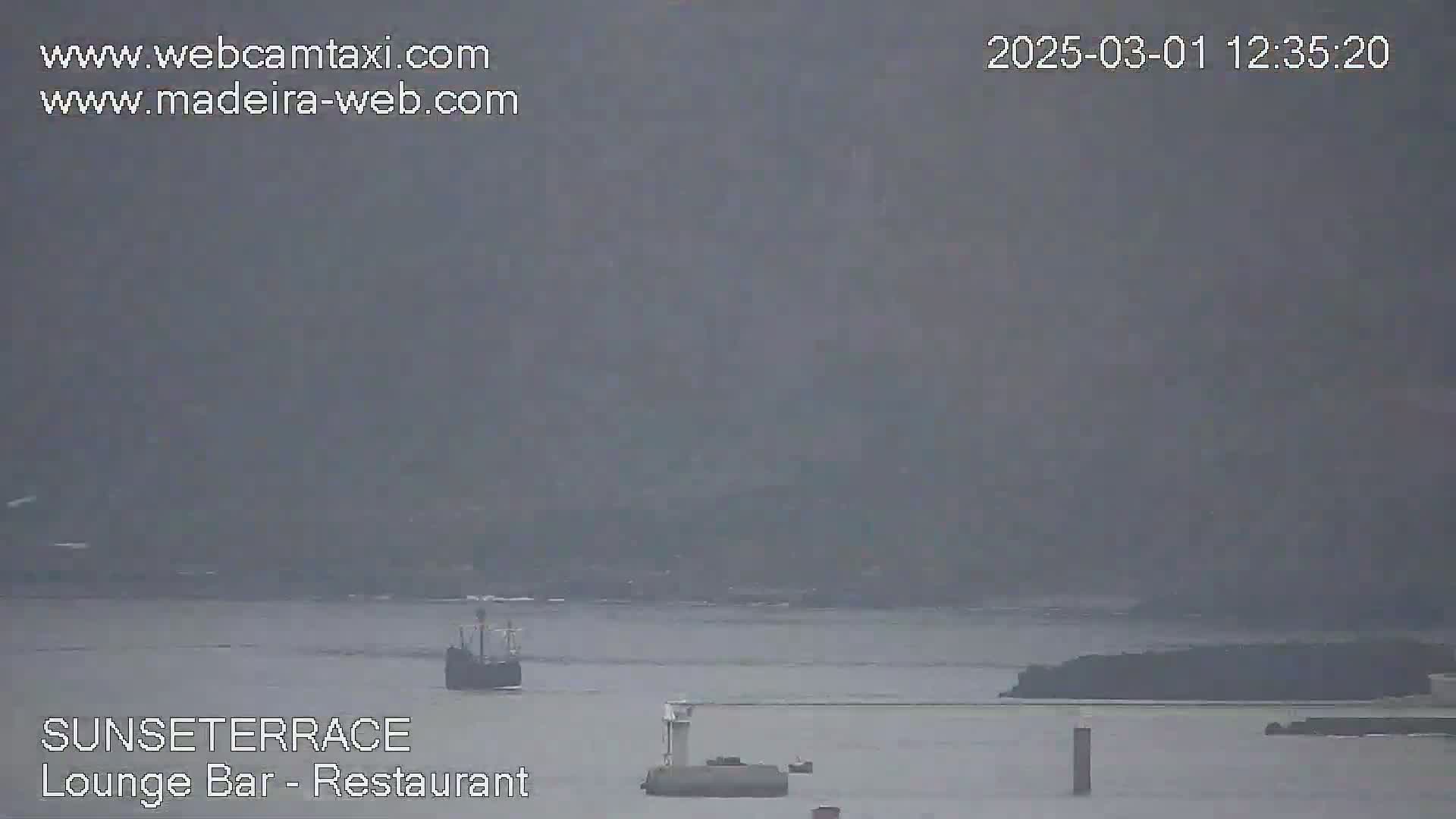 A hazy, overcast day shows a body of water with a small ship and some landmasses in the distance.