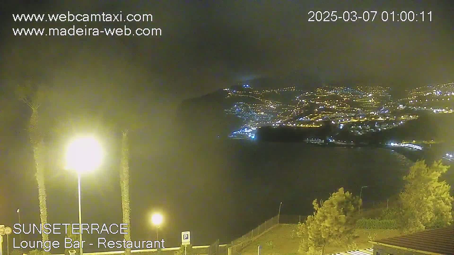 A nighttime, hazy view of a city illuminated by lights along a coastline, seen from a vantage point above.