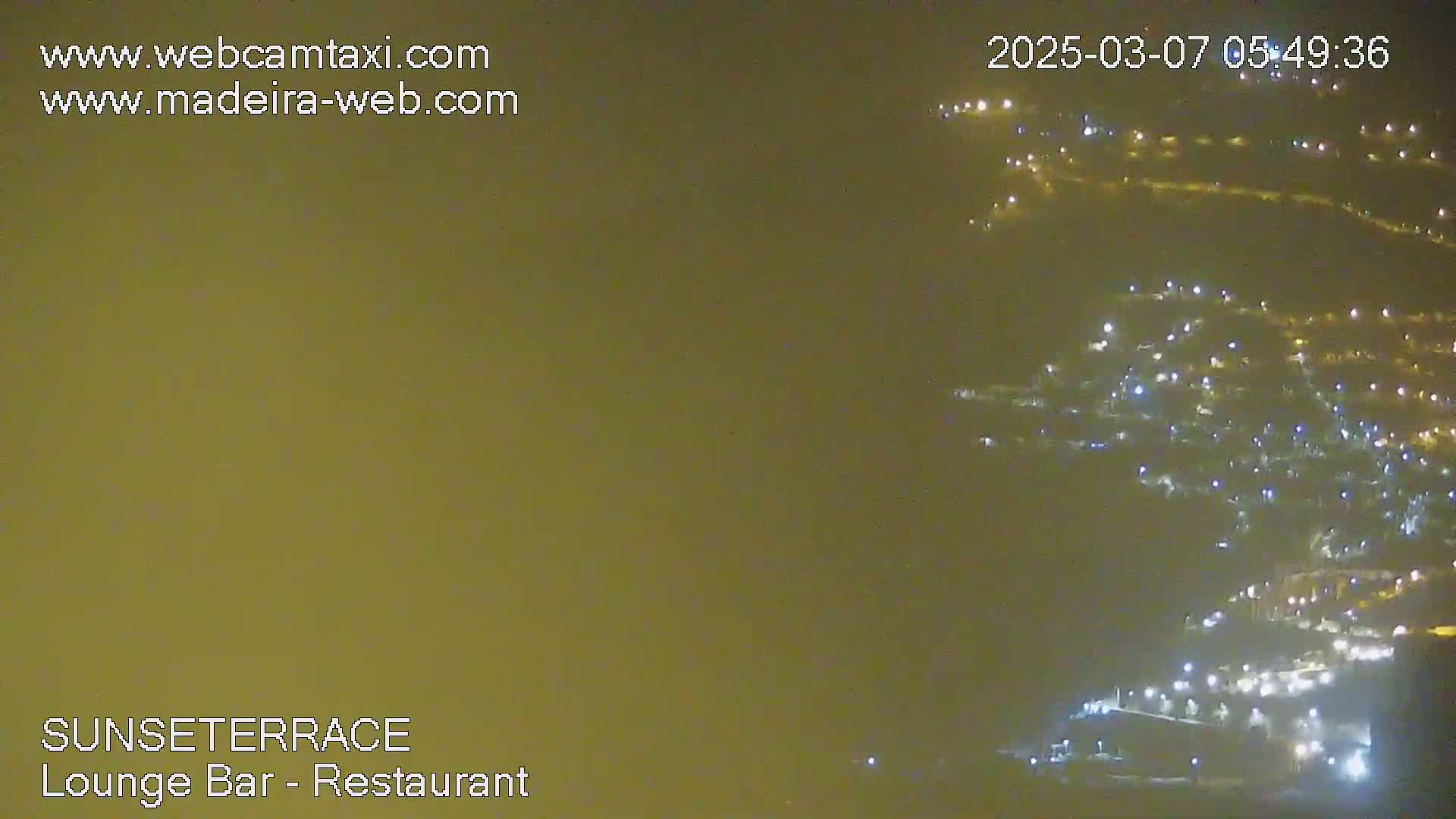 A hazy night scene shows numerous lights illuminating a hillside.