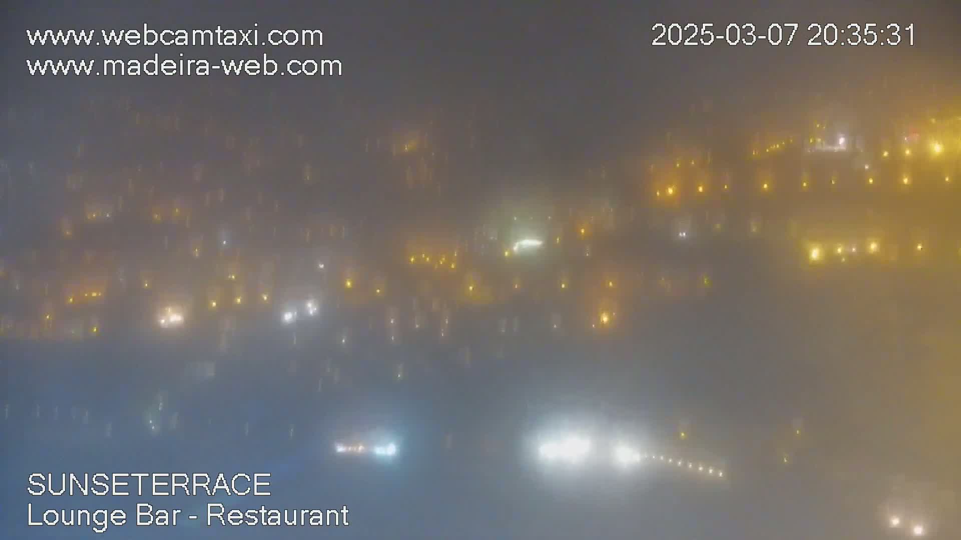 A hazy, foggy night scene shows numerous lights scattered across a landscape.
