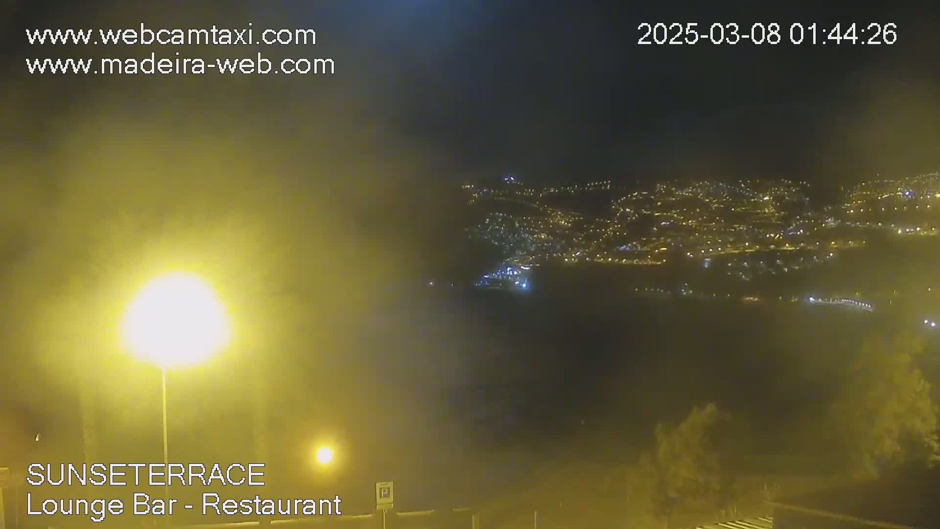 A hazy night scene shows a distant town glowing with lights below a dark, possibly foggy sky.