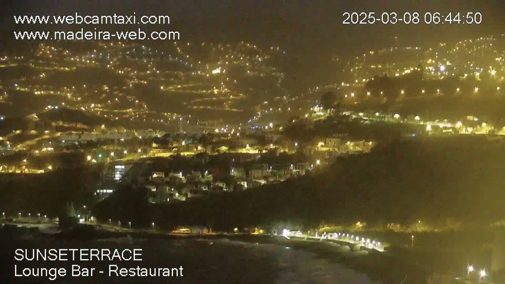 A nighttime, aerial view of a hillside town illuminated by numerous lights.