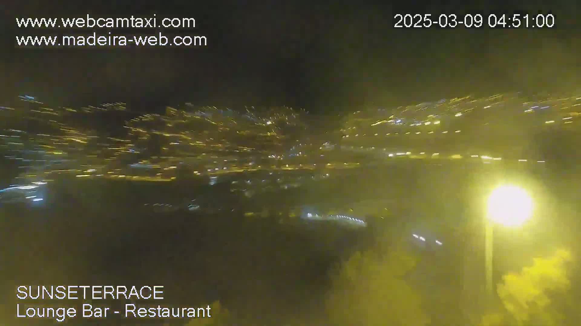 A nighttime, blurry view of a distant city illuminated with many lights under hazy conditions.