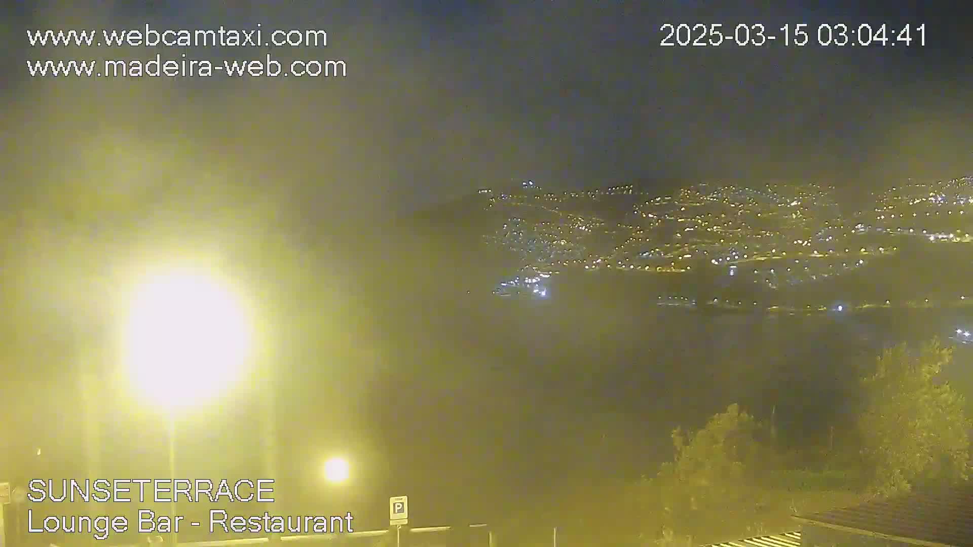 A hazy night scene shows a distant city illuminated with lights below a partly cloudy sky.