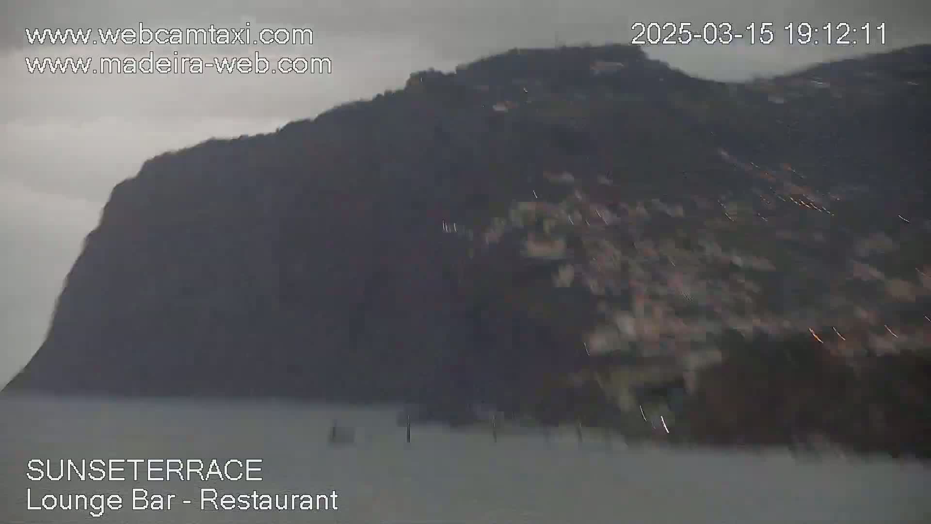 A dark, overcast day shows a large, dark cliff overlooking calm water.