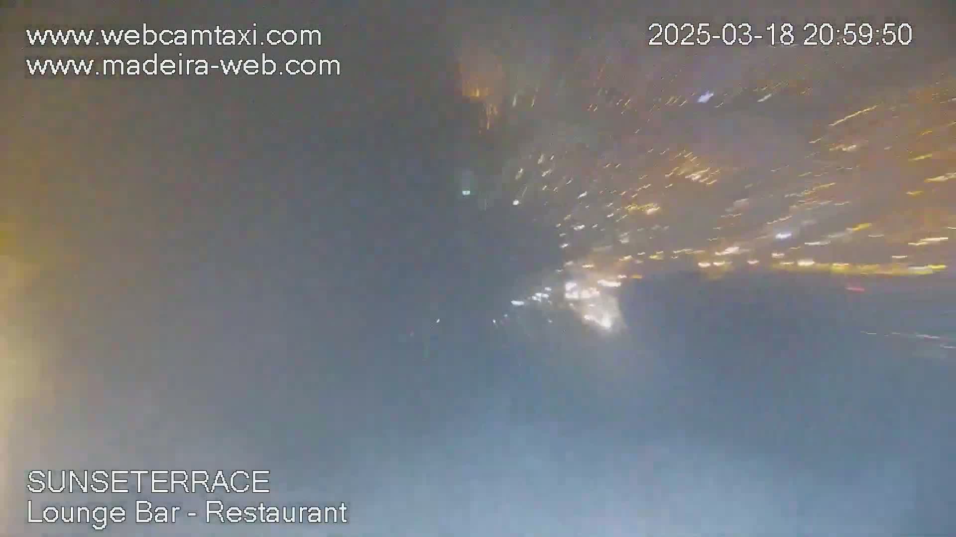 A nighttime, blurry view of bright streaks of light, possibly fireworks, in the distance against a hazy sky.