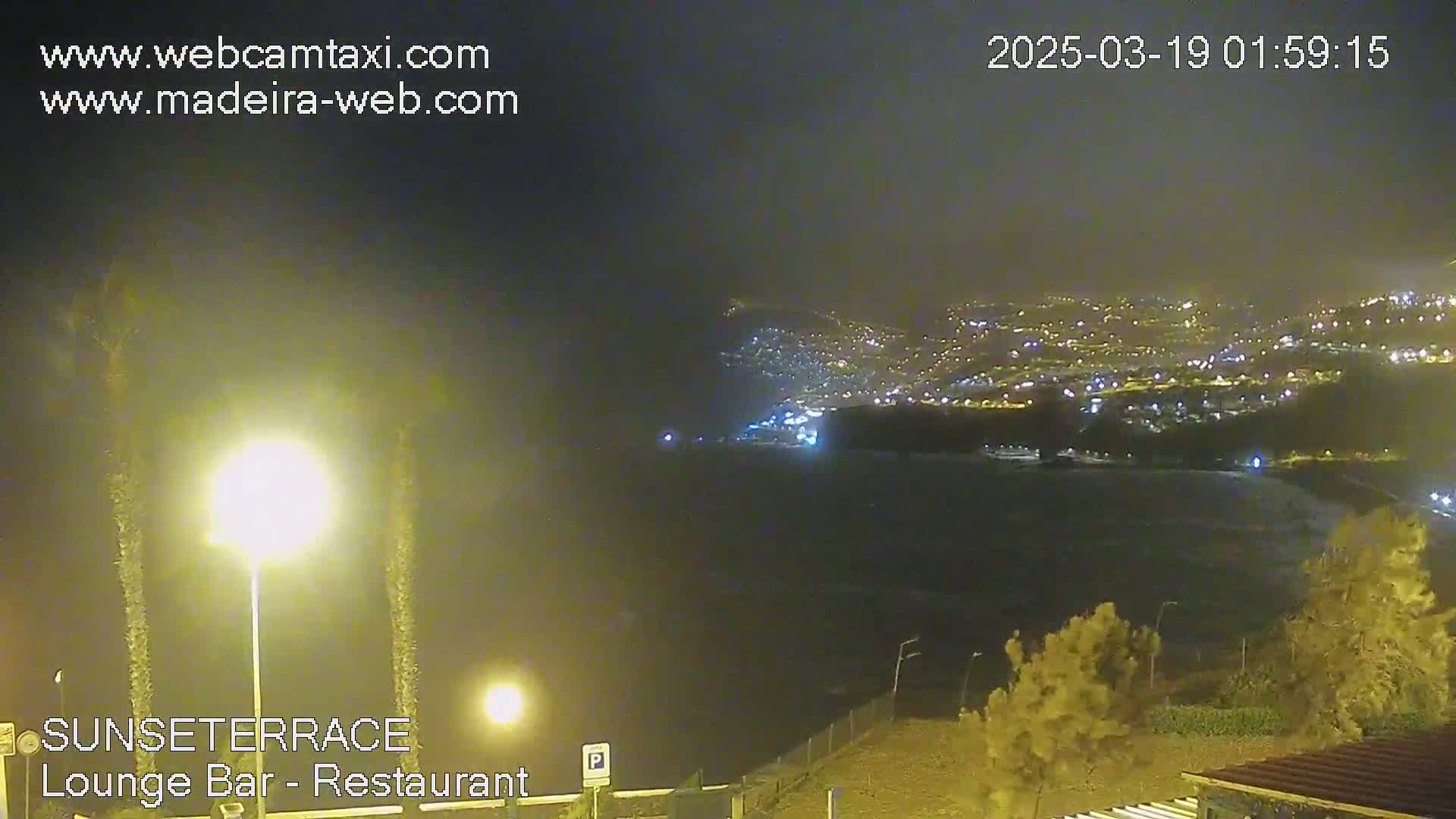 A nighttime view of a coastal city illuminated with lights under hazy or foggy conditions.