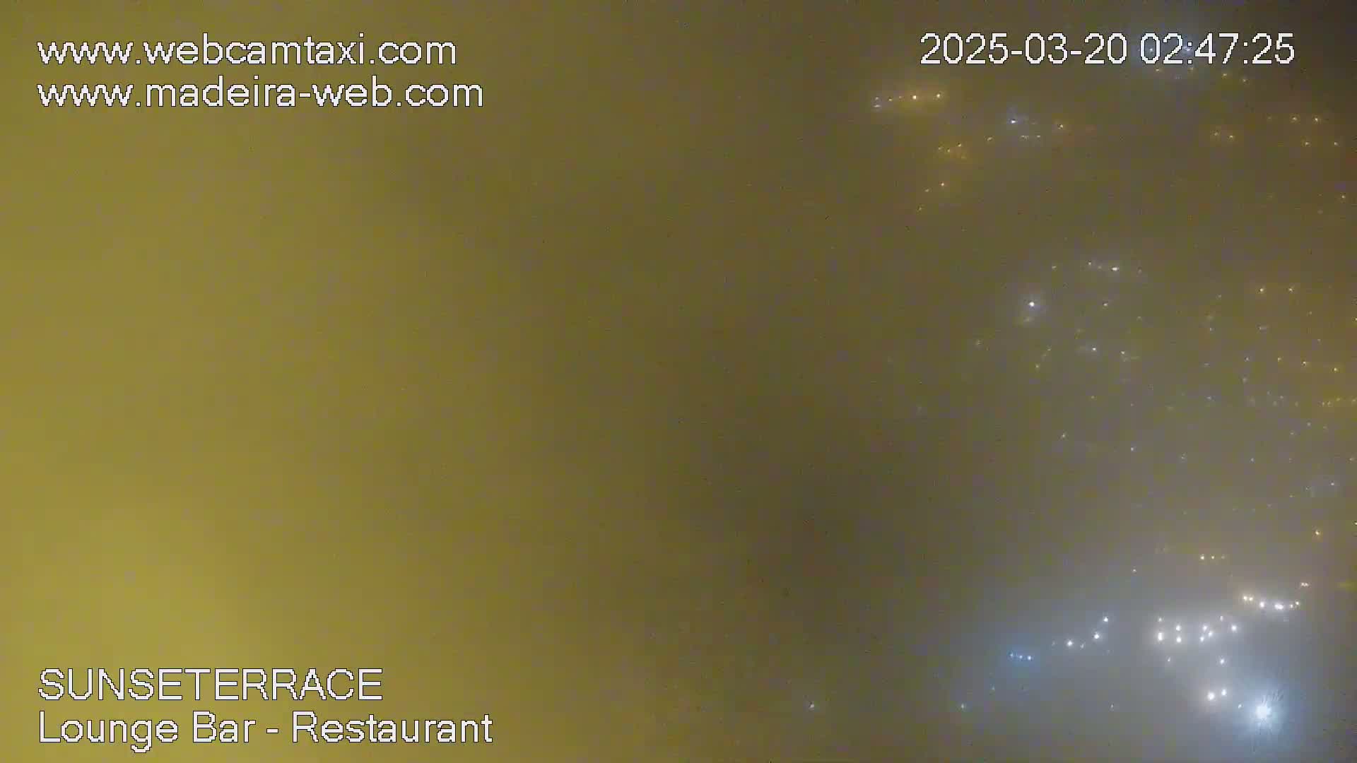 A hazy, nighttime view shows distant city lights speckled across a muted, brownish-yellow sky.