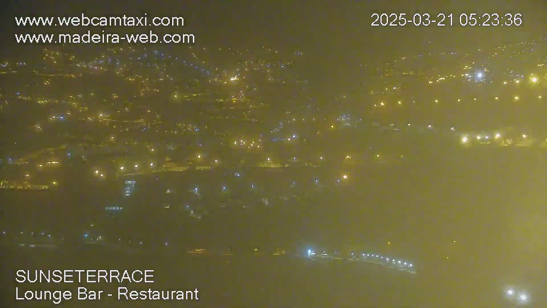 A hazy, nighttime view of a city with numerous lights scattered across a wide area.