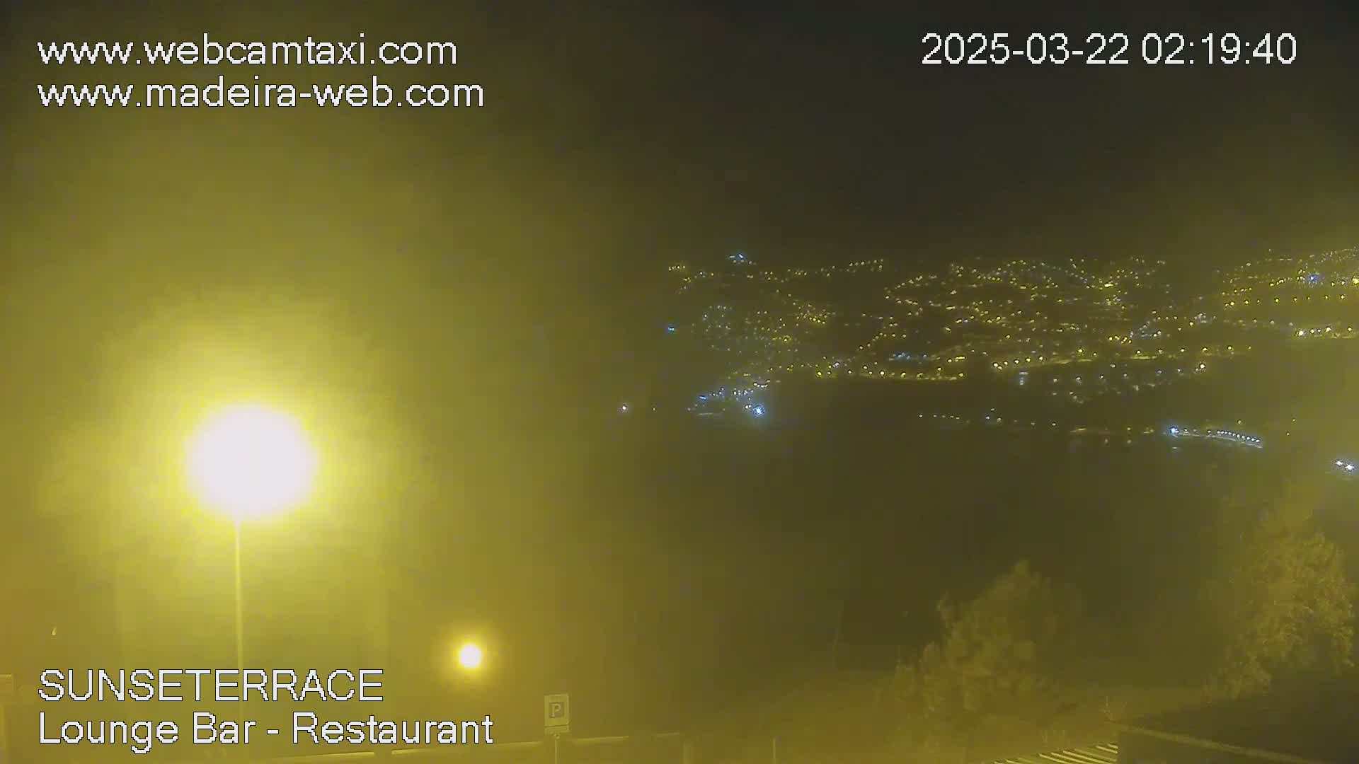 A hazy night scene shows a distant city illuminated with lights below a muted, yellow-tinged sky.