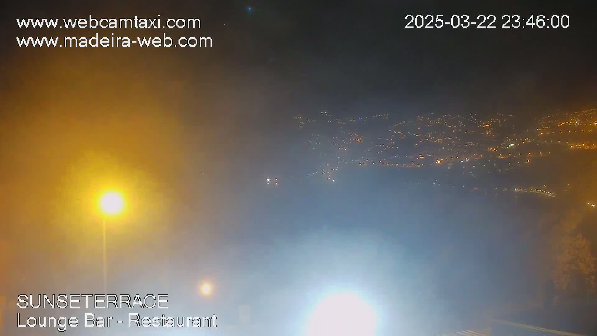 A hazy night scene shows a distant city illuminated by many lights below a bright, hazy sky.