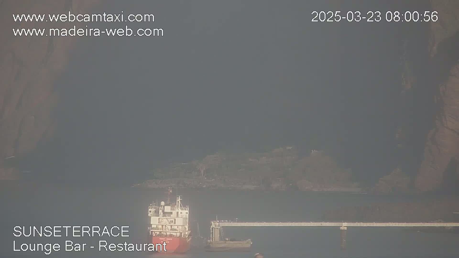 A hazy view shows a ship docked at a pier near a landmass.