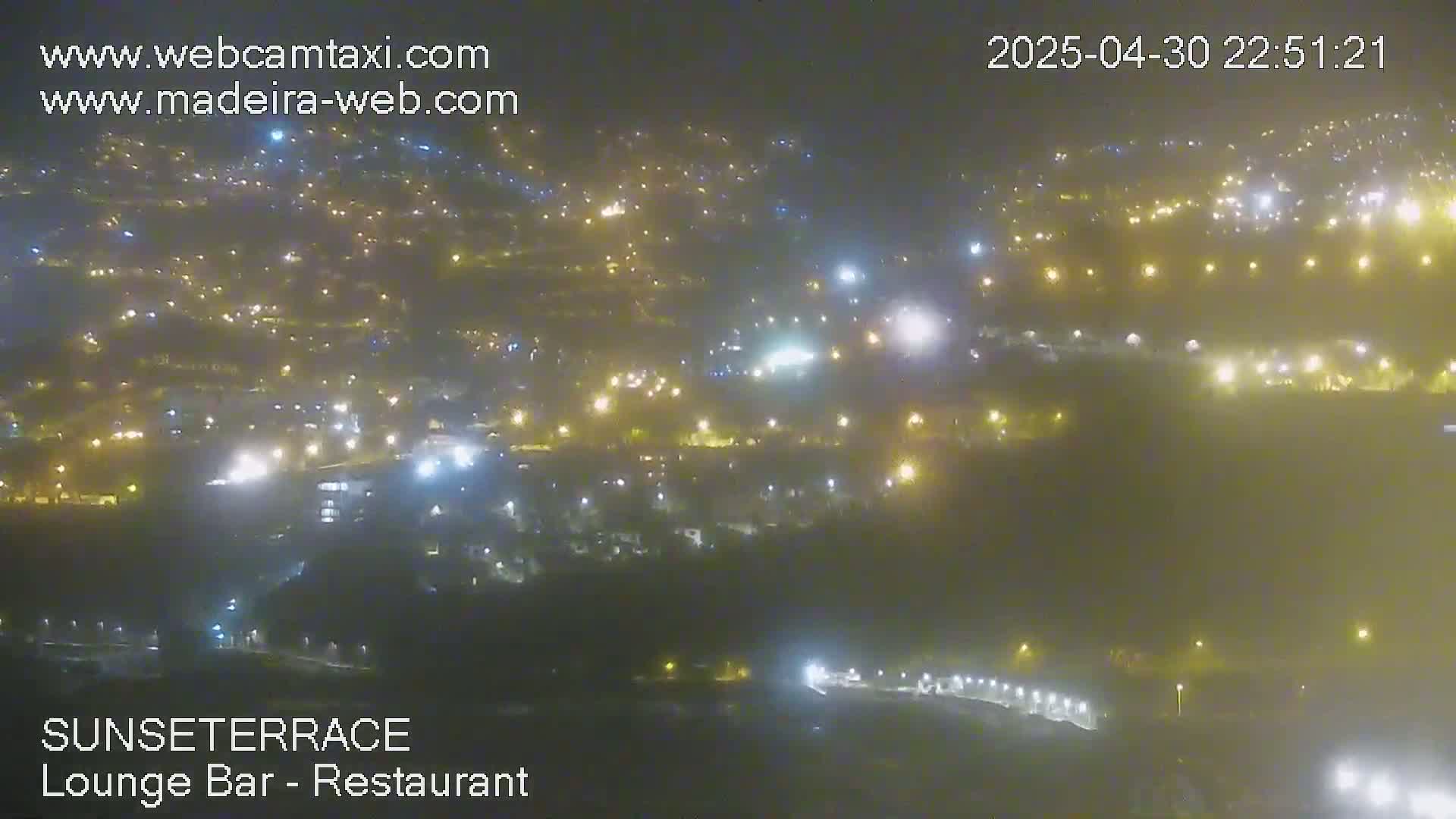 A hazy night view shows a town with many lights spread across a hillside.